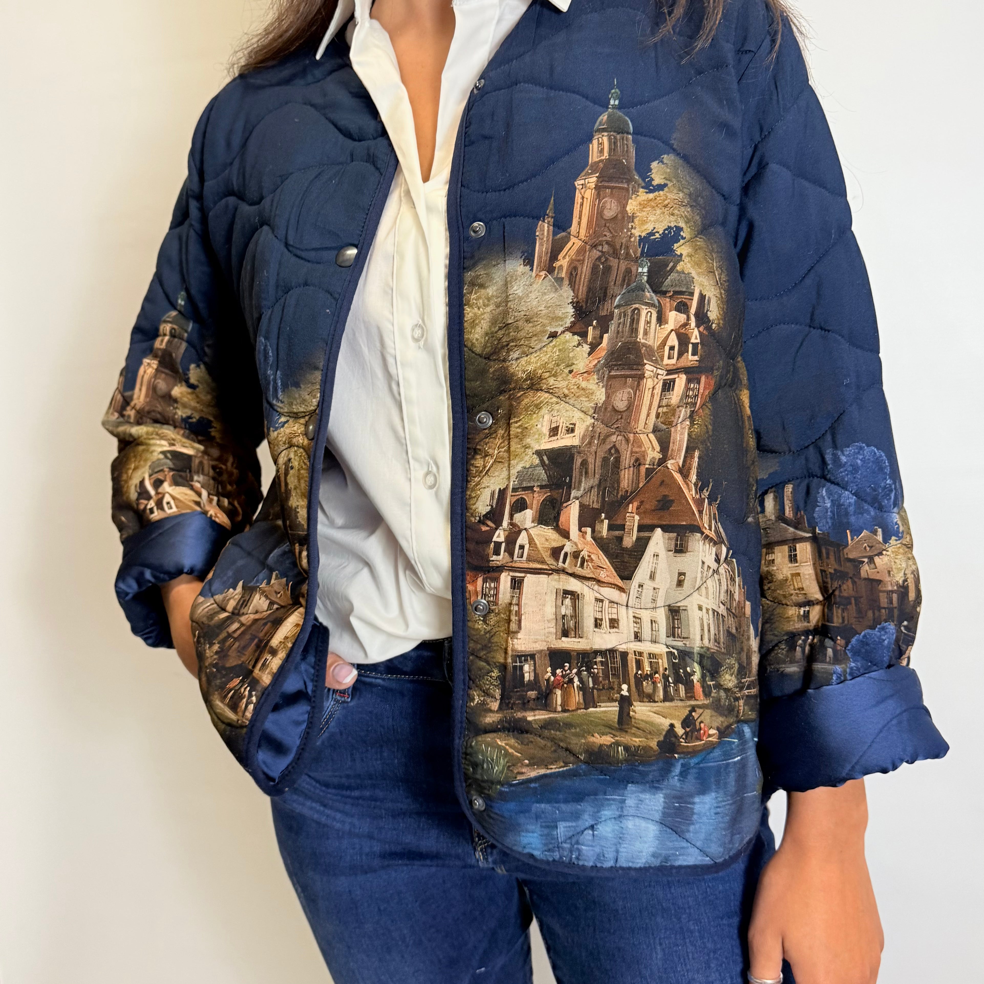 Person wearing a blue quilted jacket with a scenic print on a plain background