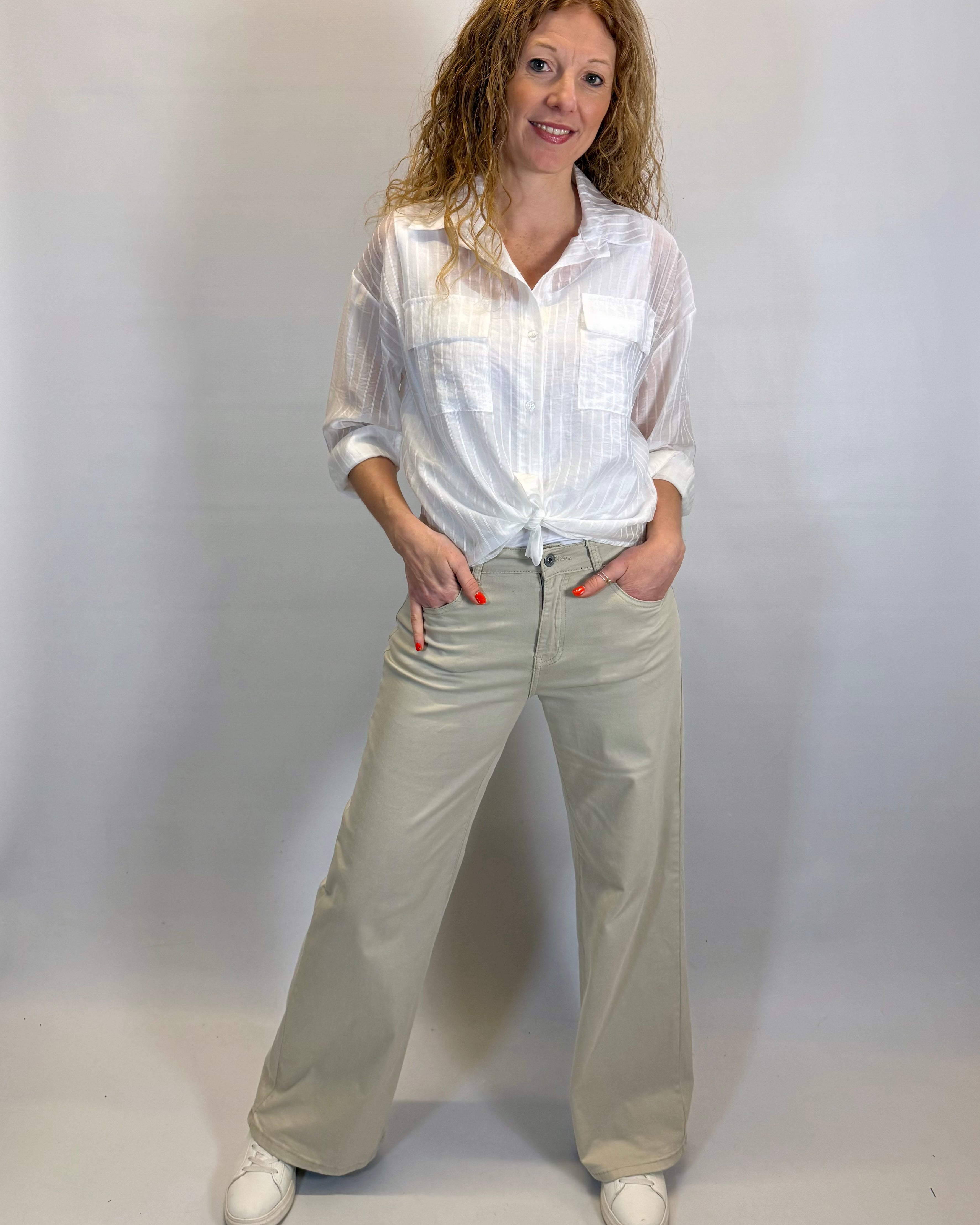 Woman wearing a white shirt and beige pants against a plain background