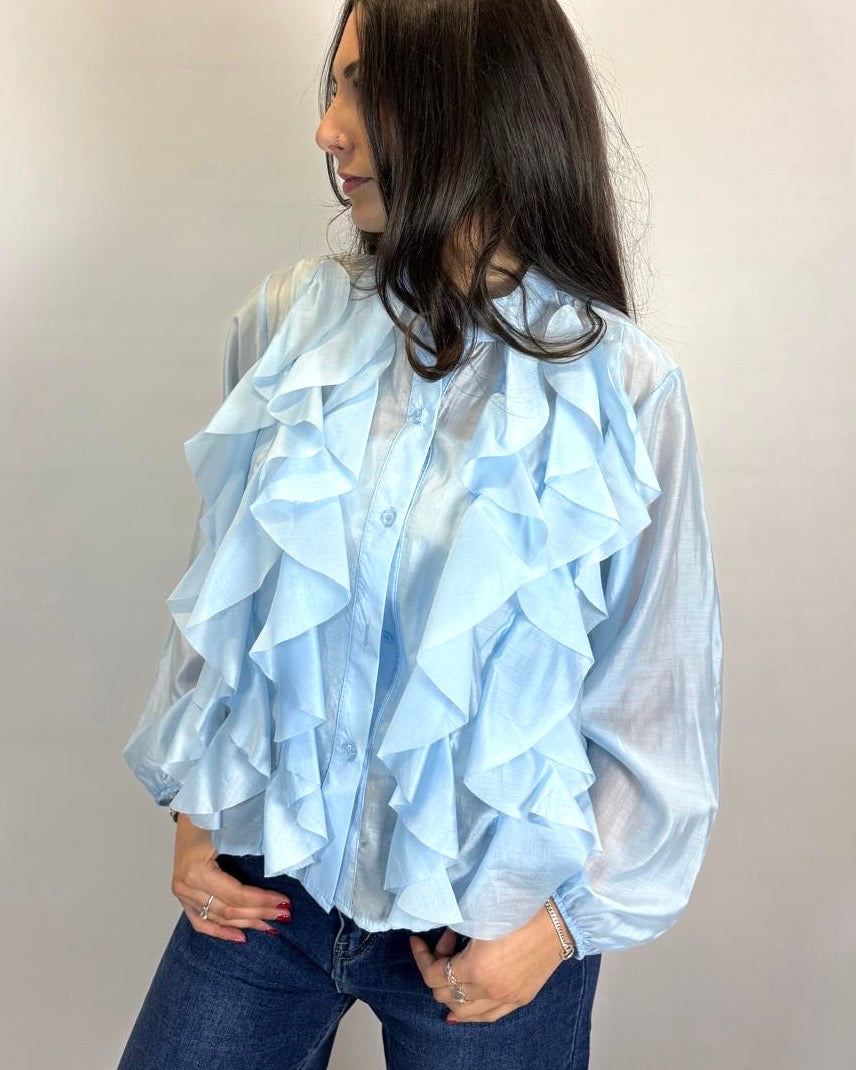 Woman wearing a light blue ruffled blouse against a plain background