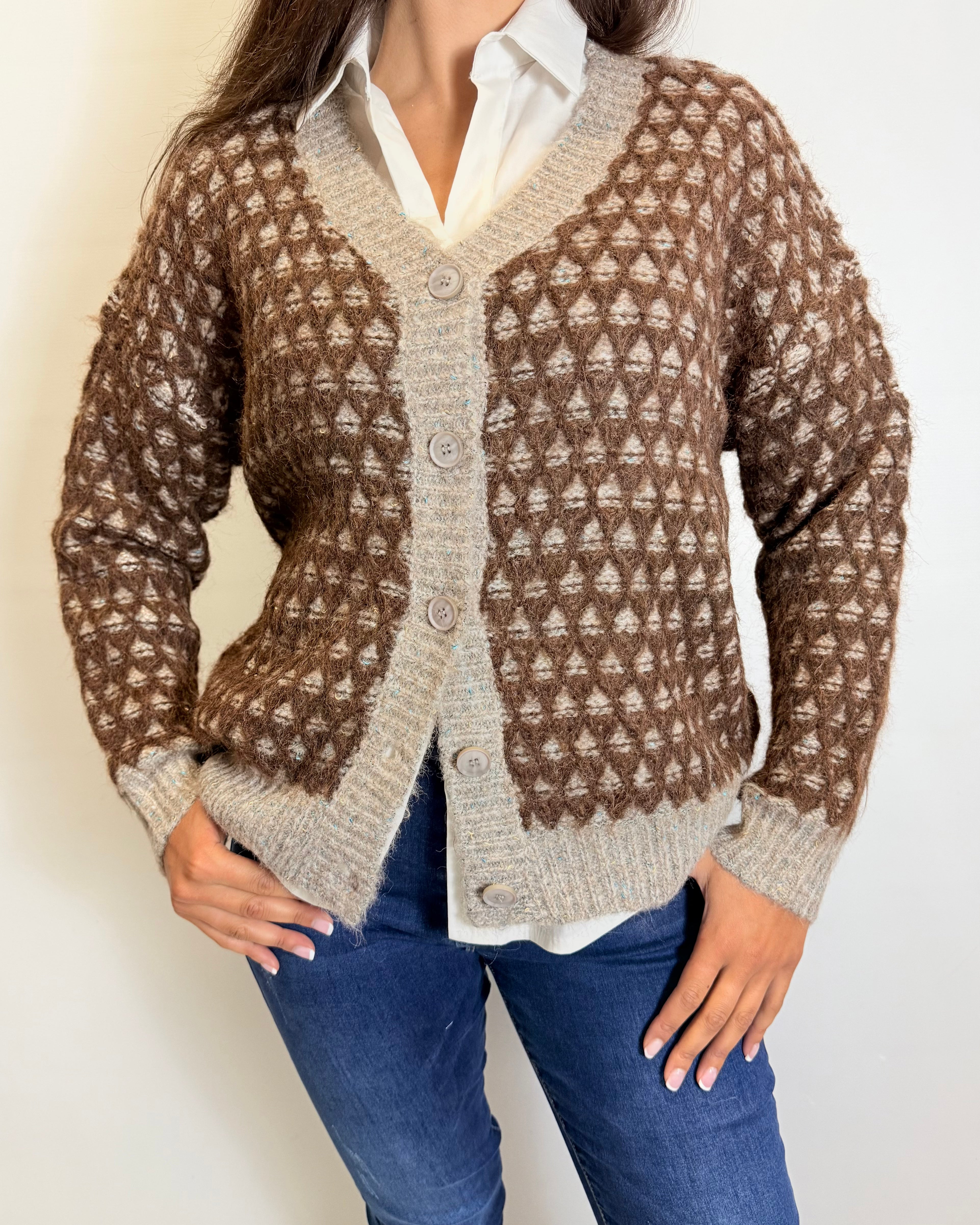 Person wearing a brown and beige patterned cardigan over a white shirt and blue jeans on a plain background