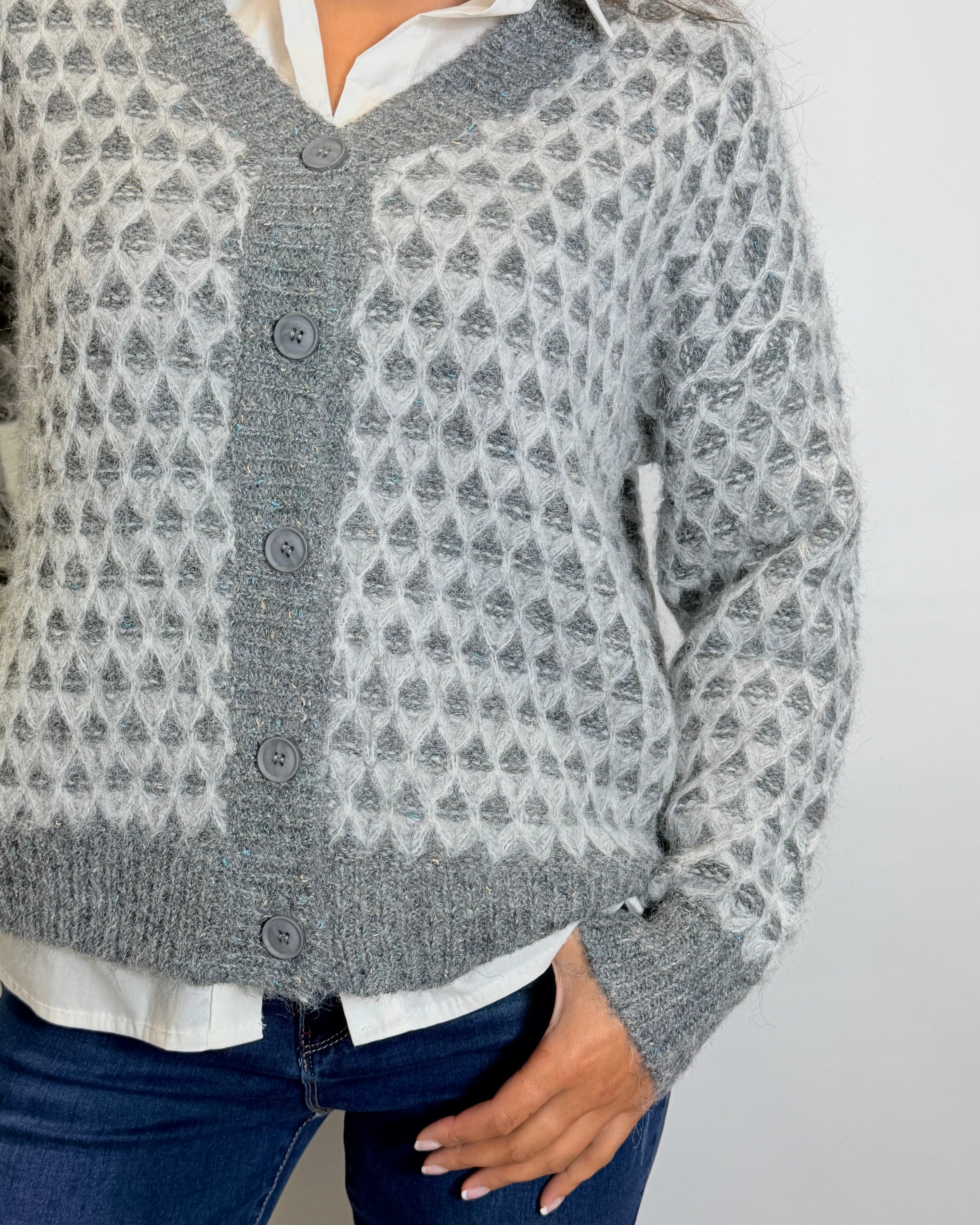 Person wearing a patterned gray cardigan over a white shirt with a plain background