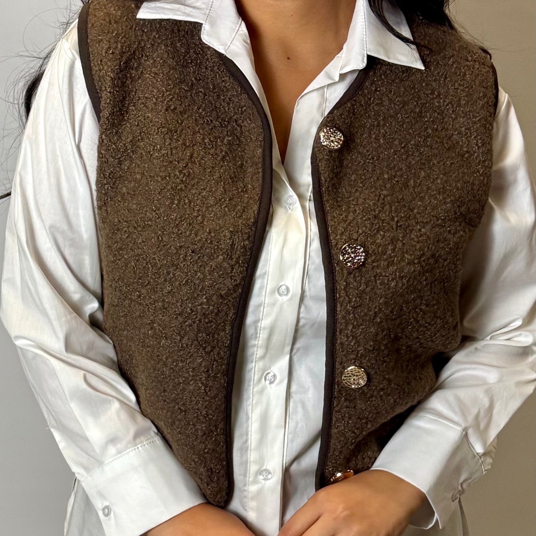 Person wearing a brown vest over a white shirt with a neutral background