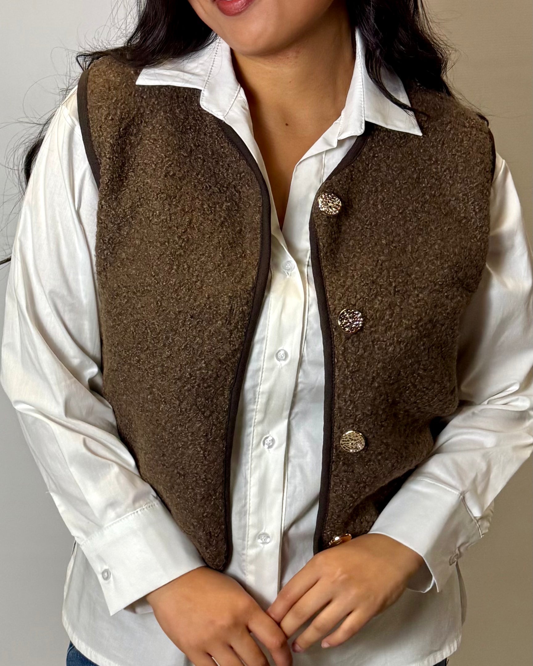Person wearing a brown vest over a white shirt with a neutral background