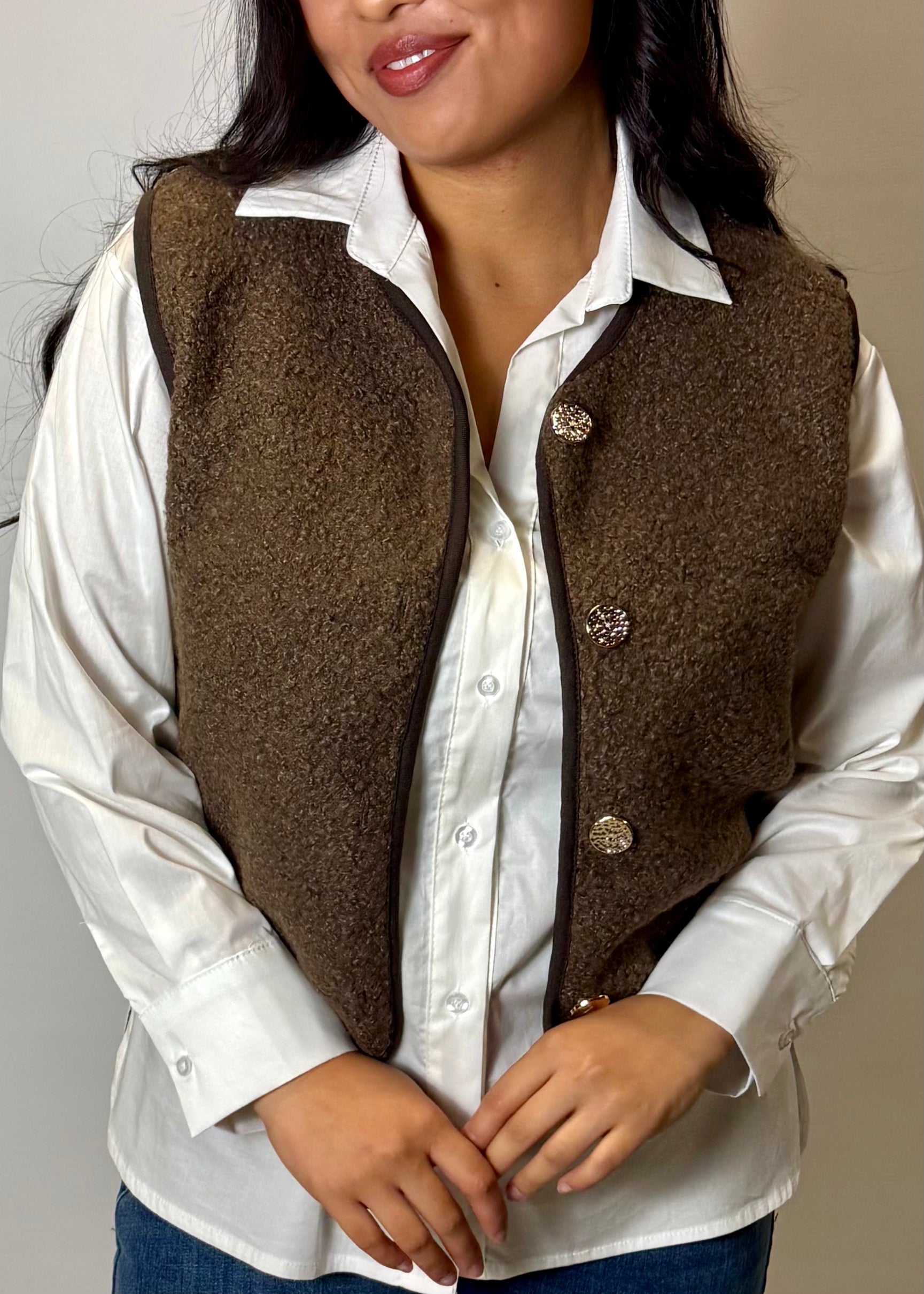 Person wearing a brown vest over a white shirt with a neutral background