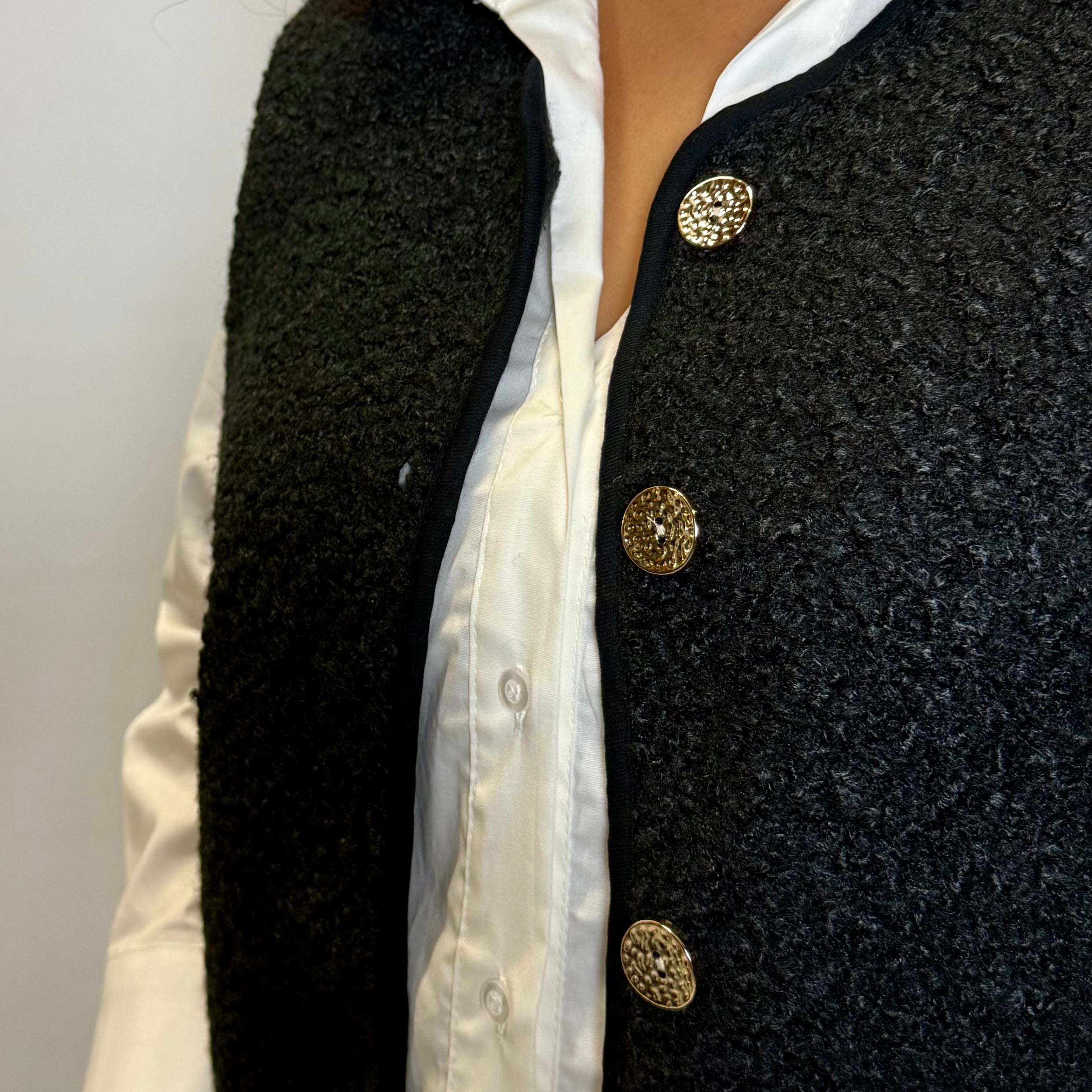 Black textured vest with gold buttons over a white shirt on a plain background