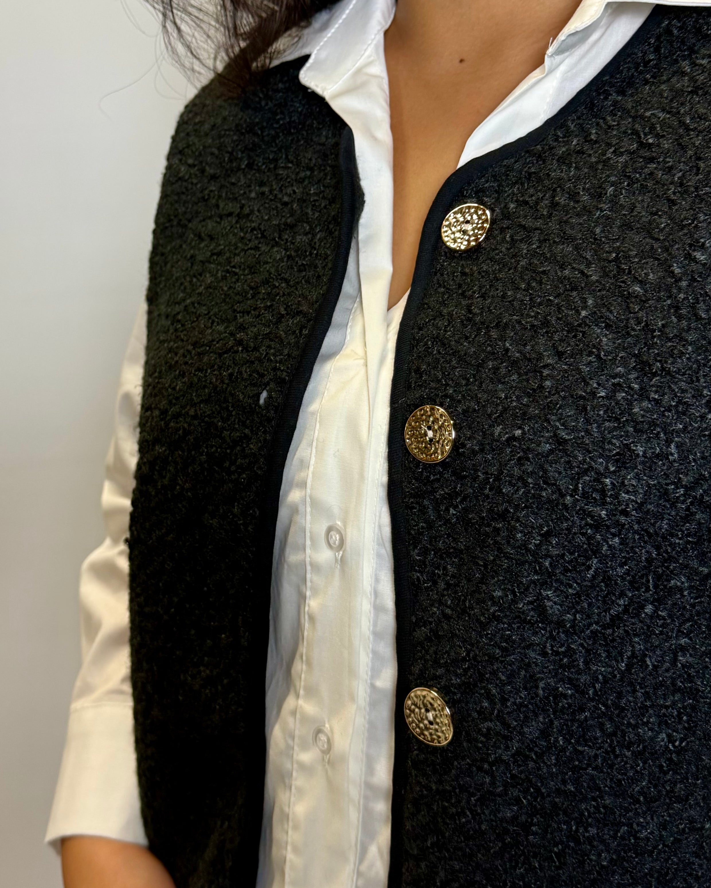 Black textured vest with gold buttons over a white shirt on a plain background