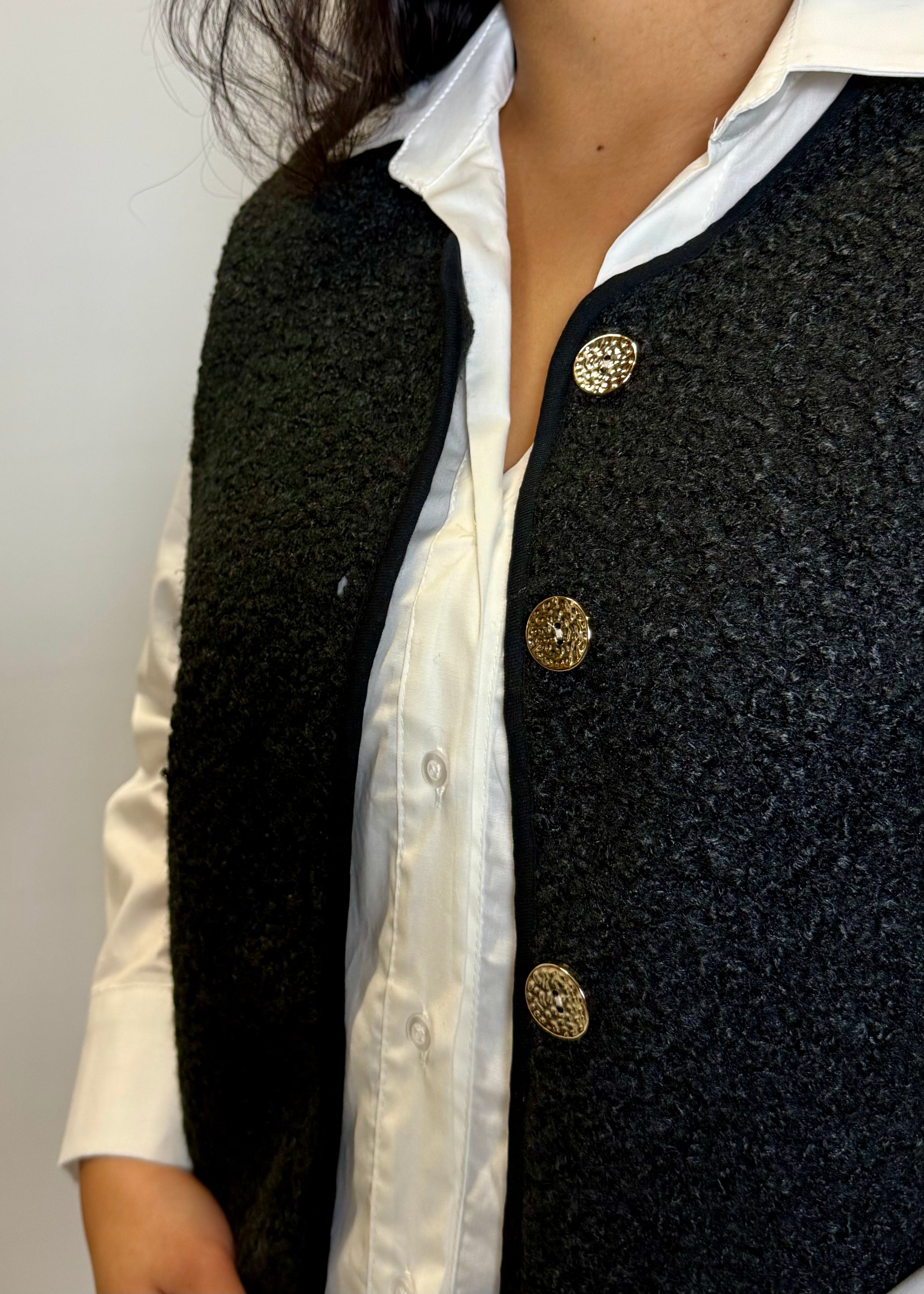 Black textured vest with gold buttons over a white shirt on a plain background
