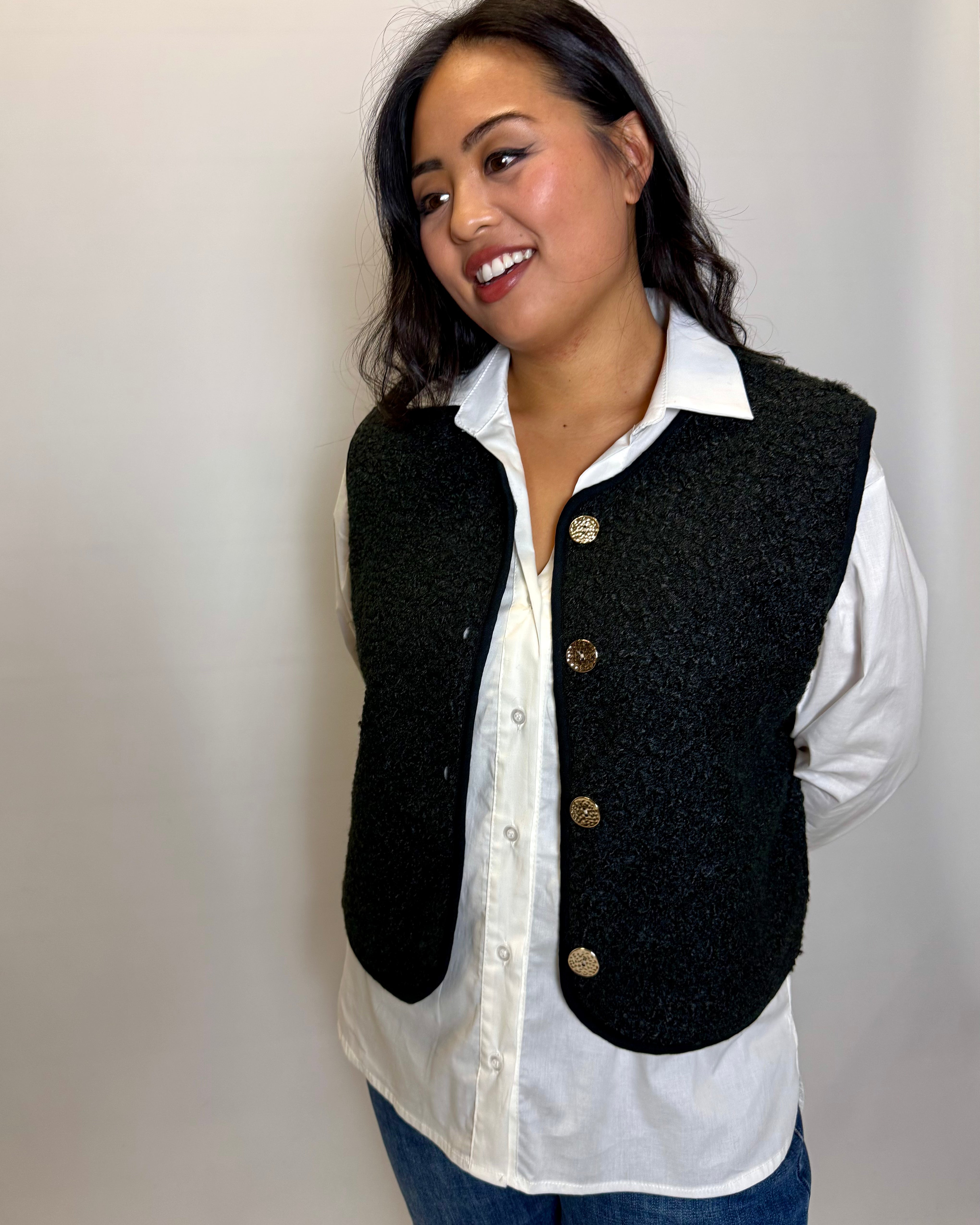 Woman wearing a black vest over a white shirt with a plain background