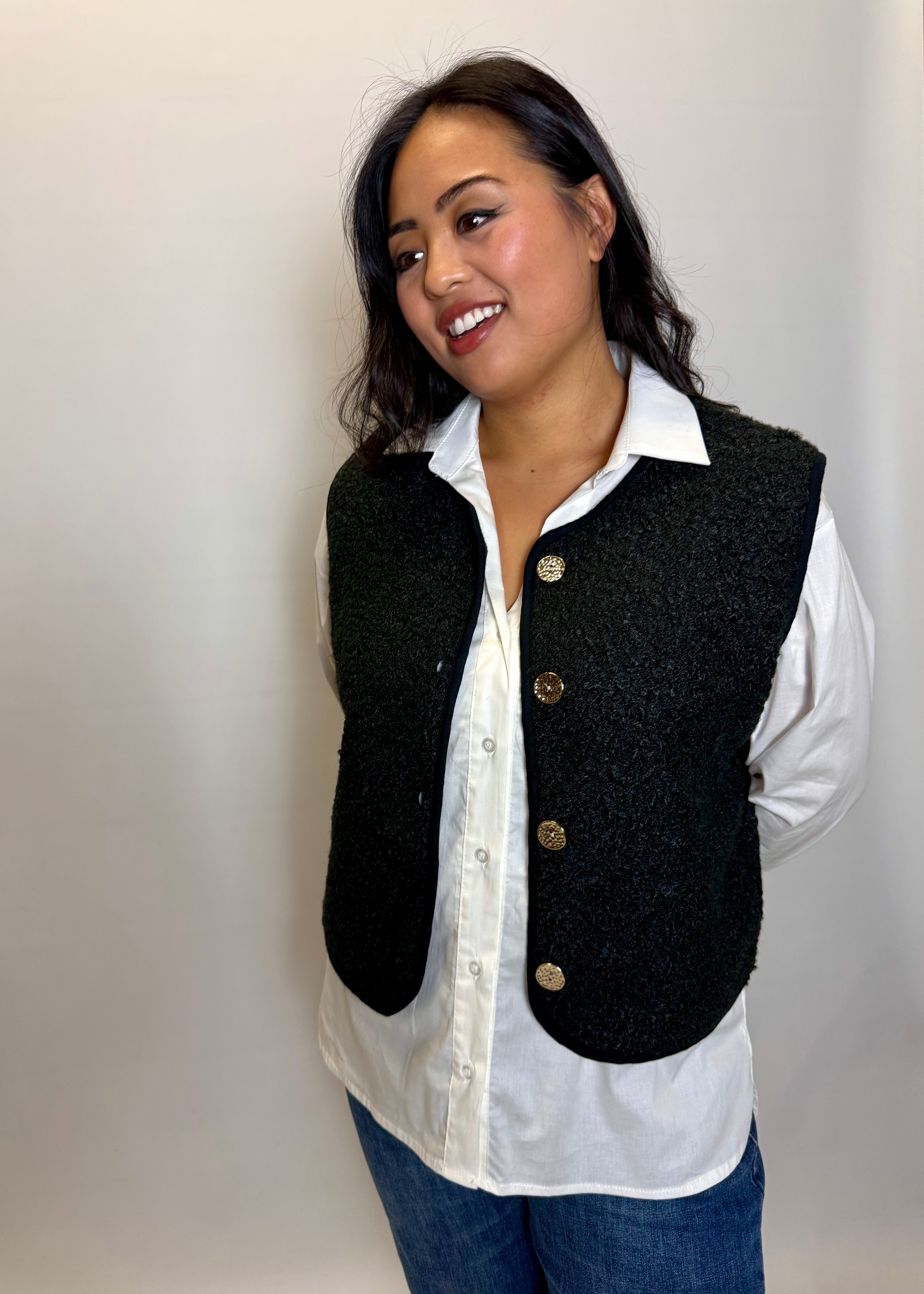 Woman wearing a black vest over a white shirt with a plain background