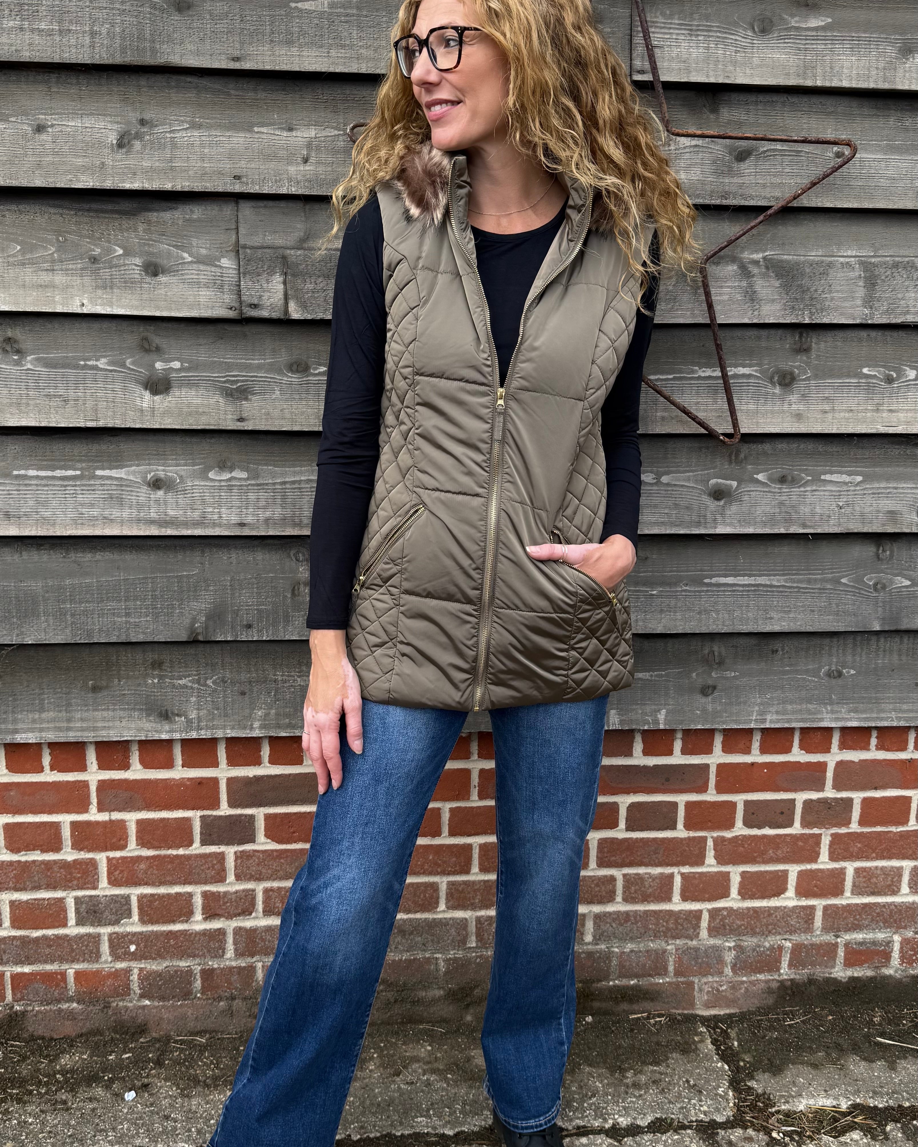 Woman wearing a puffer vest standing against a wooden wall.