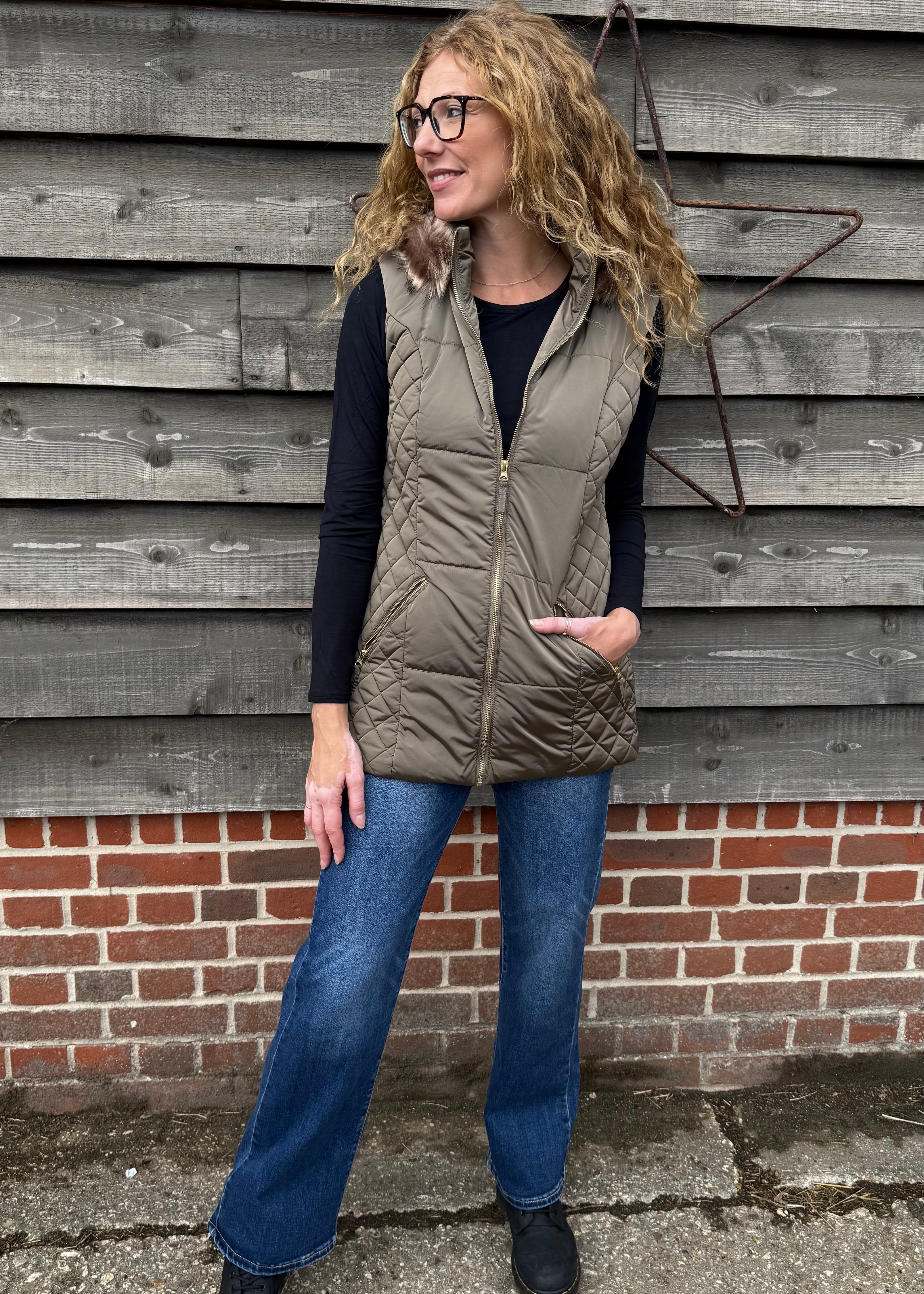 Woman wearing a puffer vest standing against a wooden wall.