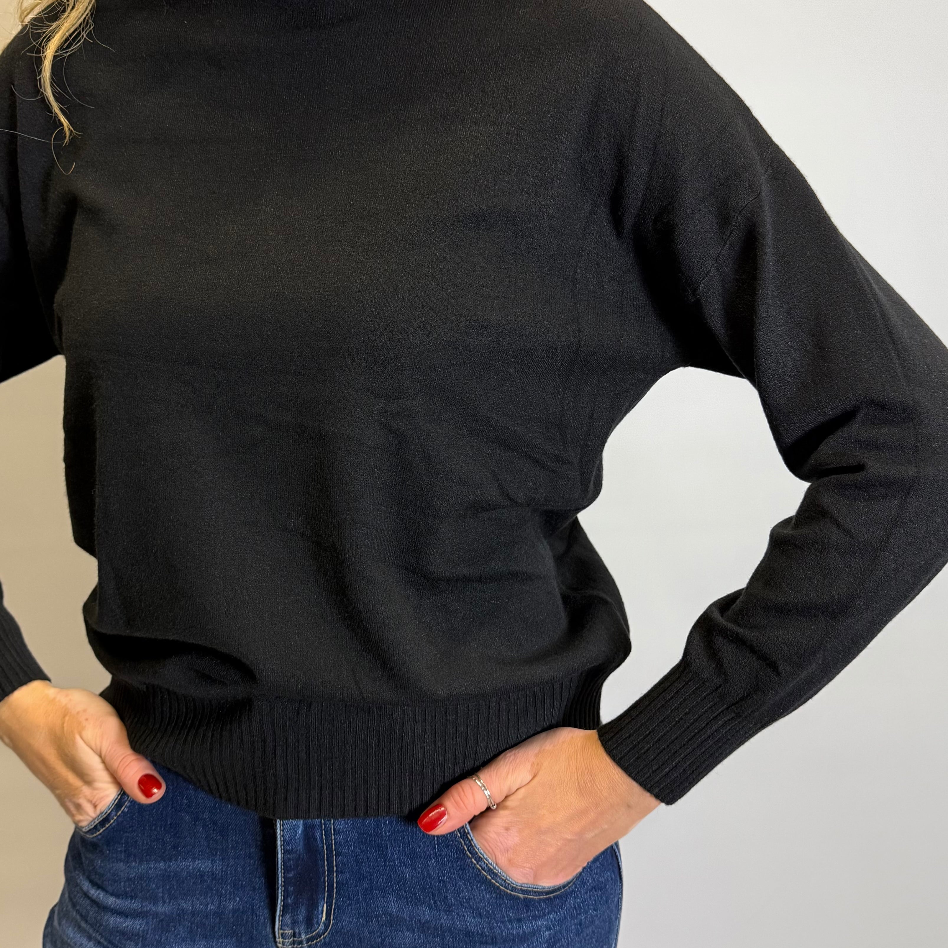 Person wearing a black sweater and blue jeans on a plain background