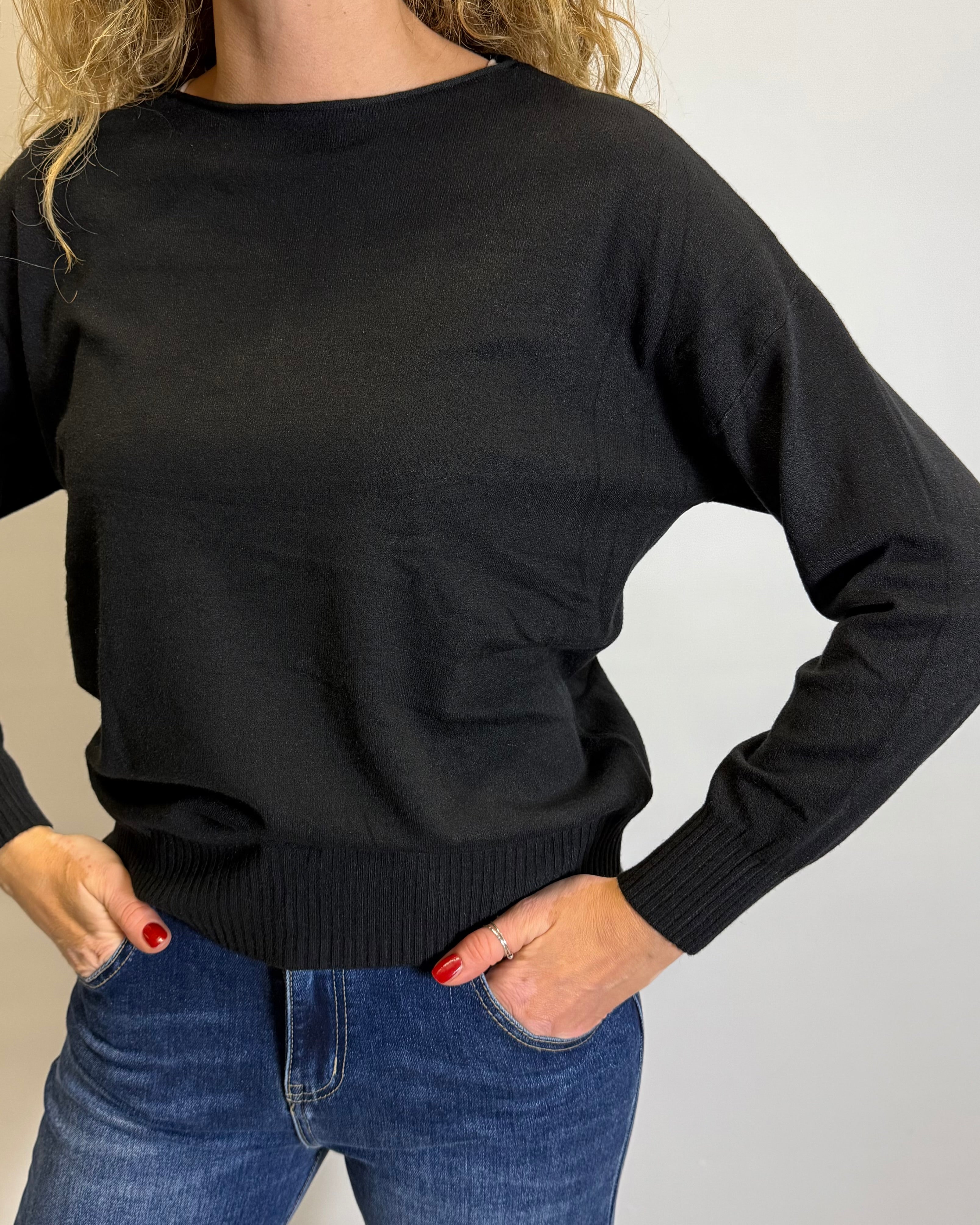 Person wearing a black sweater and blue jeans on a plain background