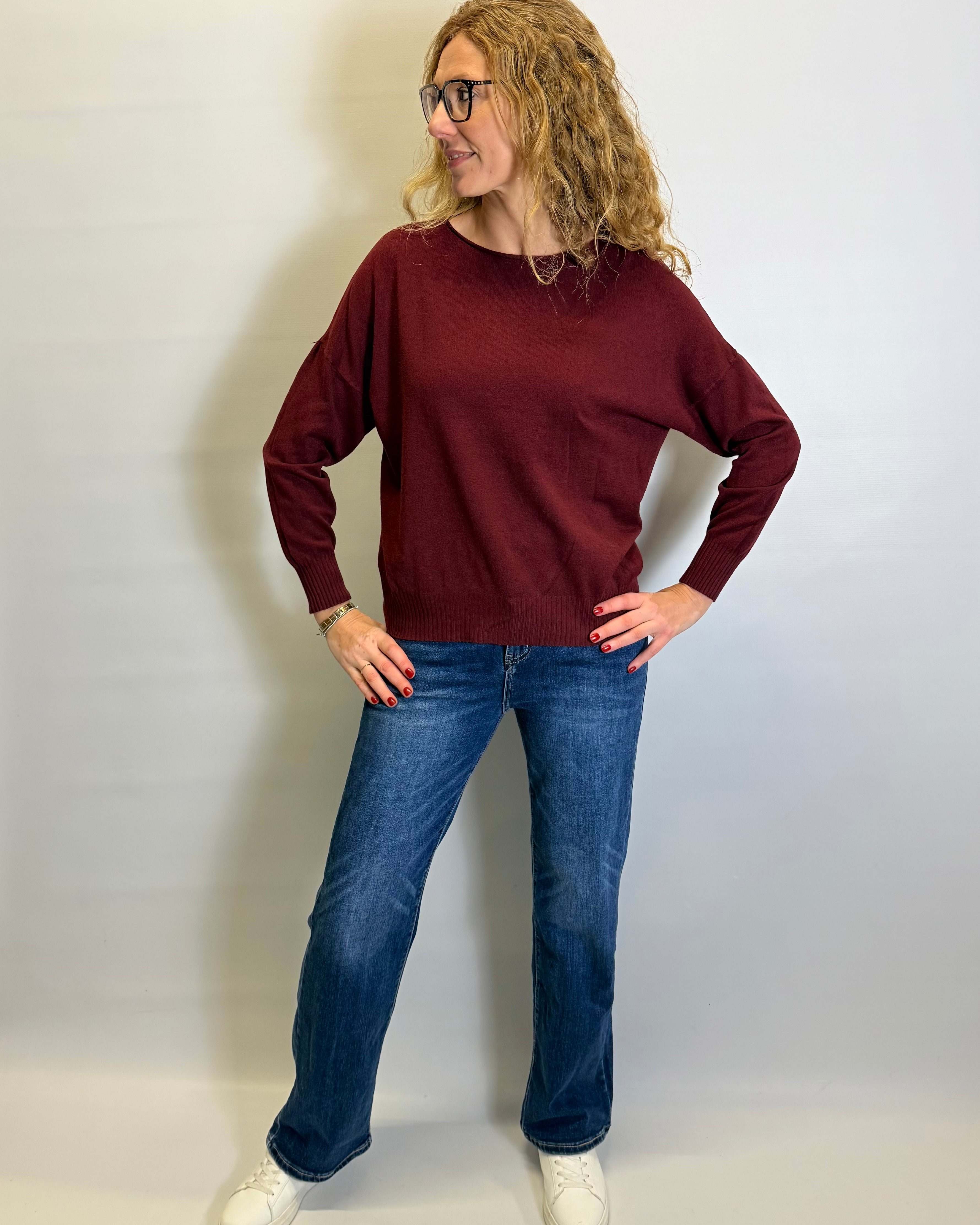 Woman wearing a burgundy sweater and blue jeans against a white background