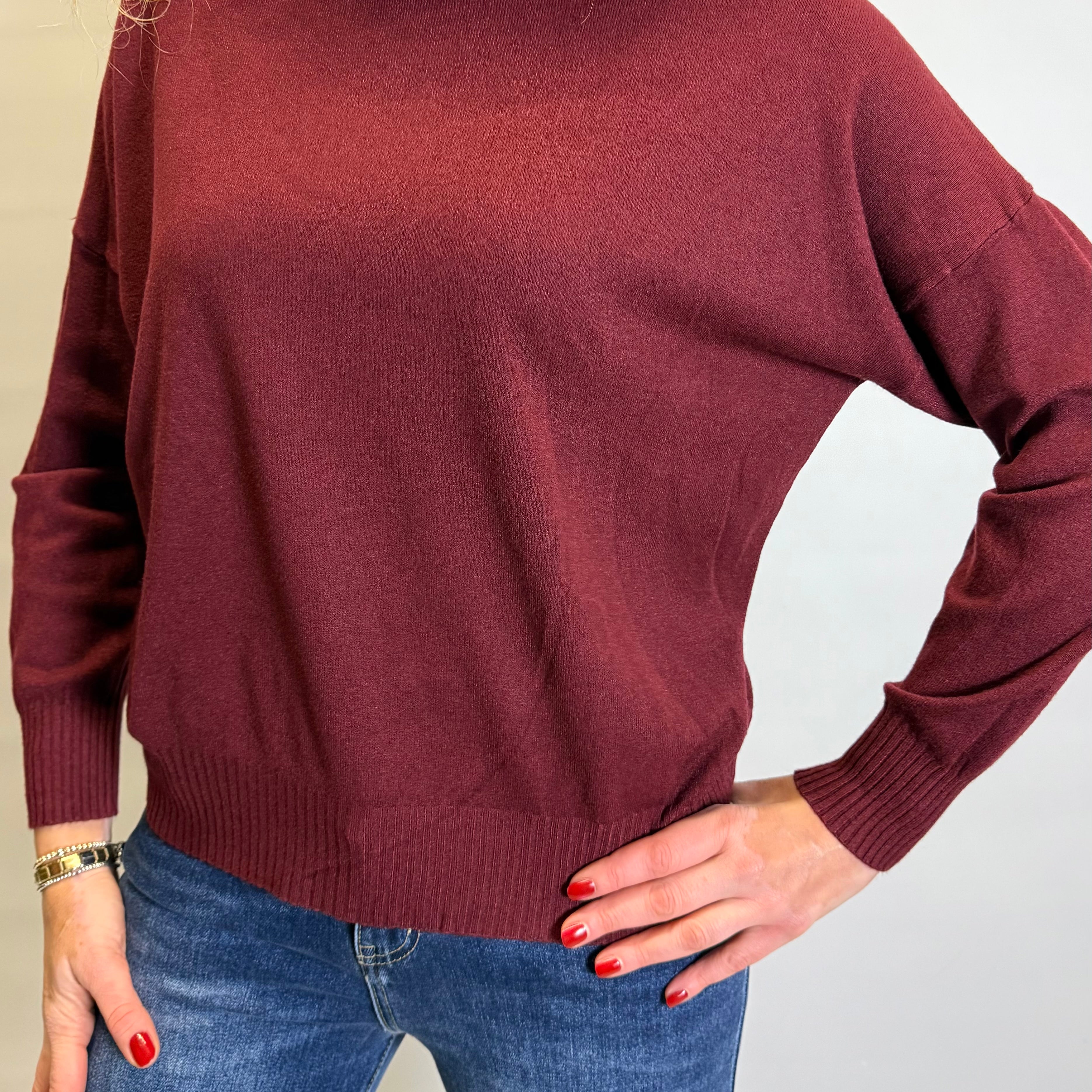 Person wearing a burgundy sweater and blue jeans against a plain background