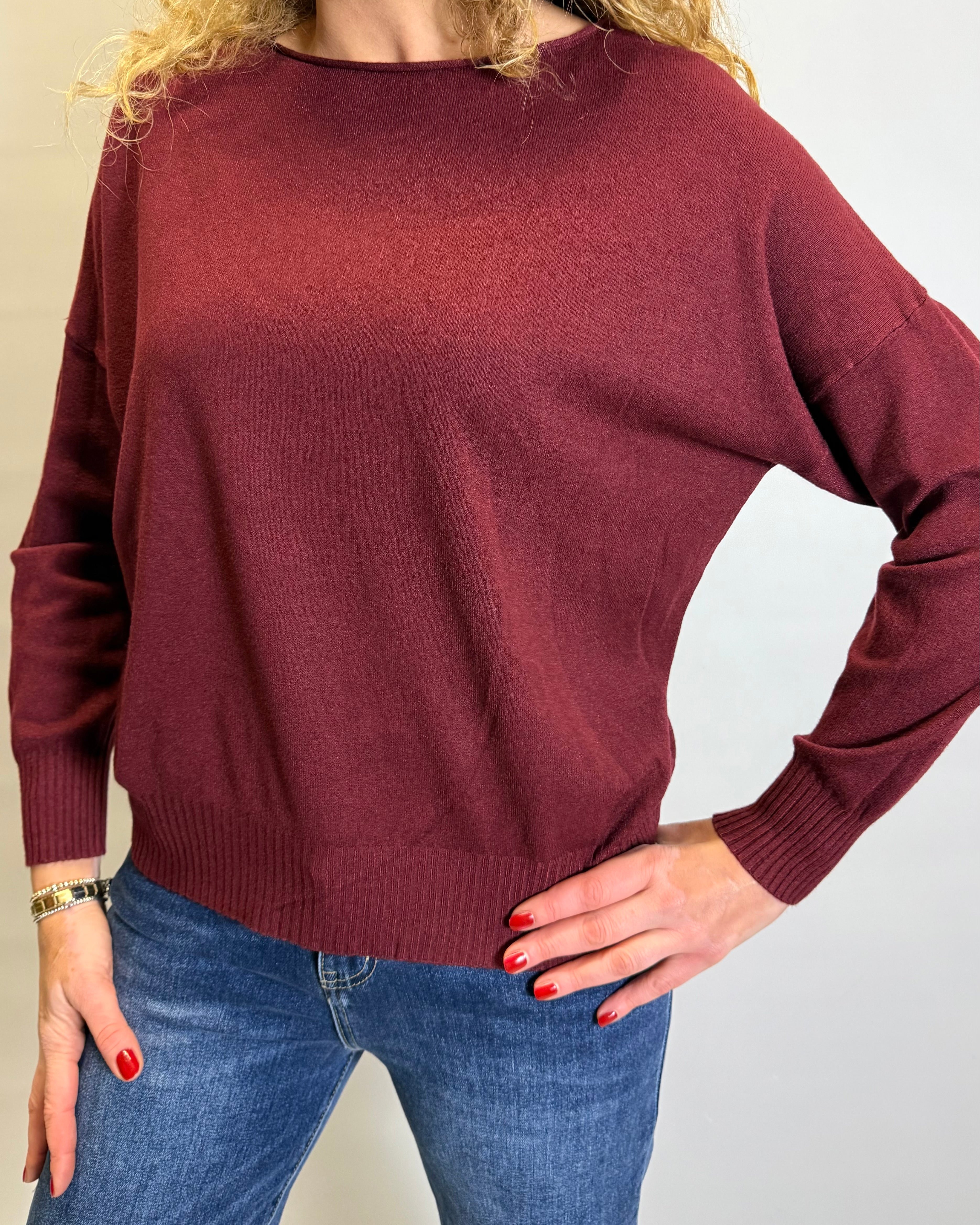 Person wearing a burgundy sweater and blue jeans against a plain background