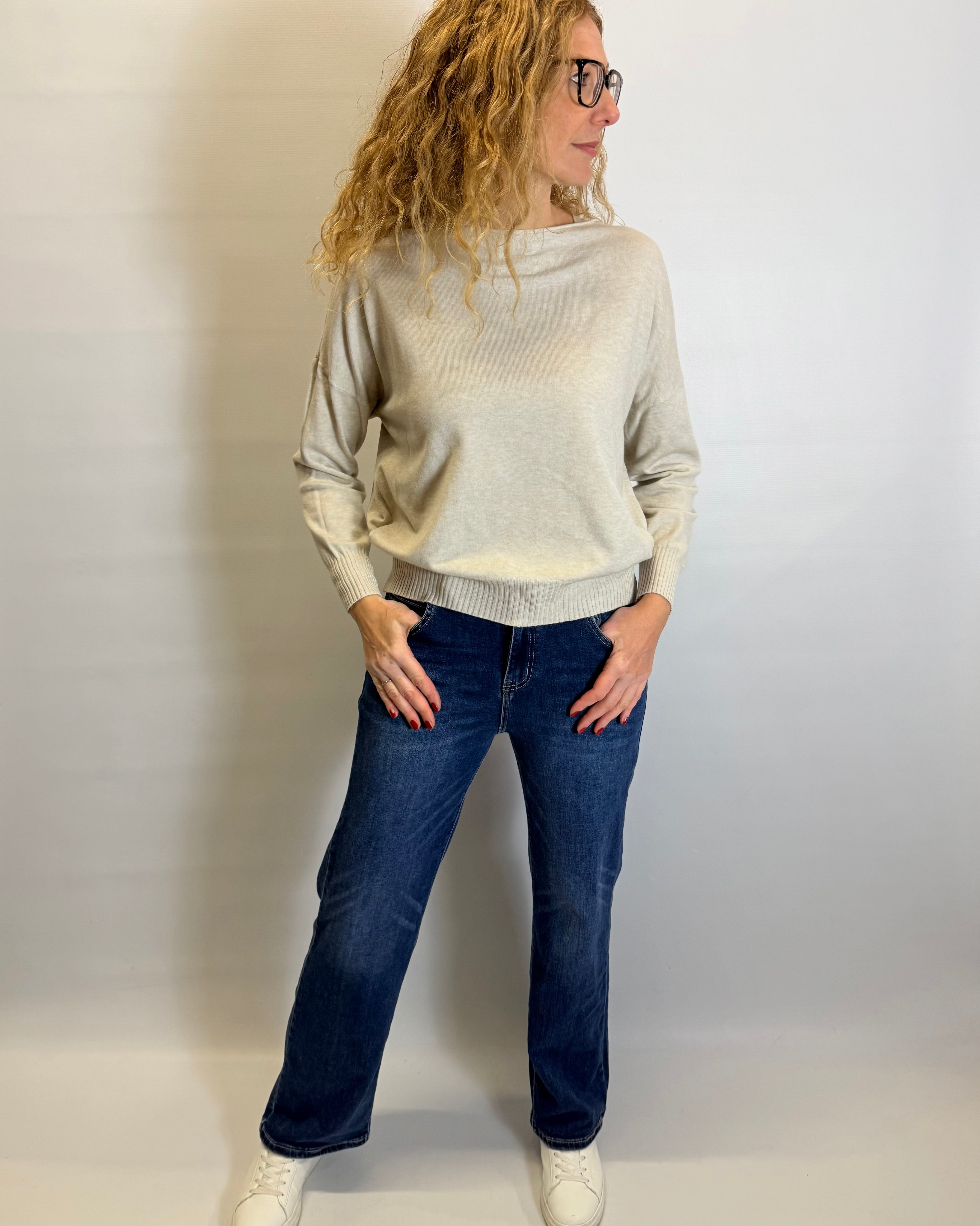 Person wearing a beige sweater and blue jeans against a plain background