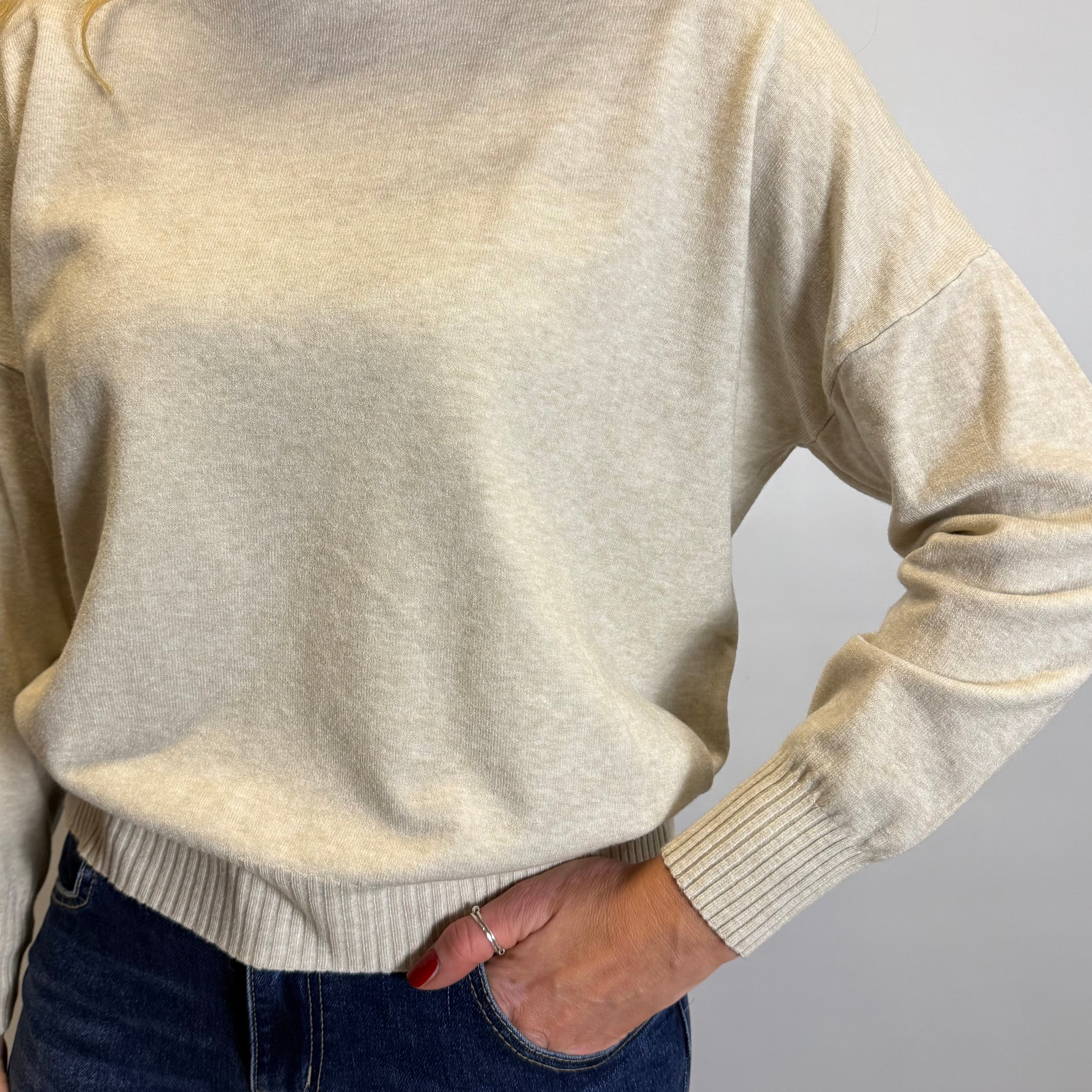 Person wearing a beige sweater and blue jeans against a plain background