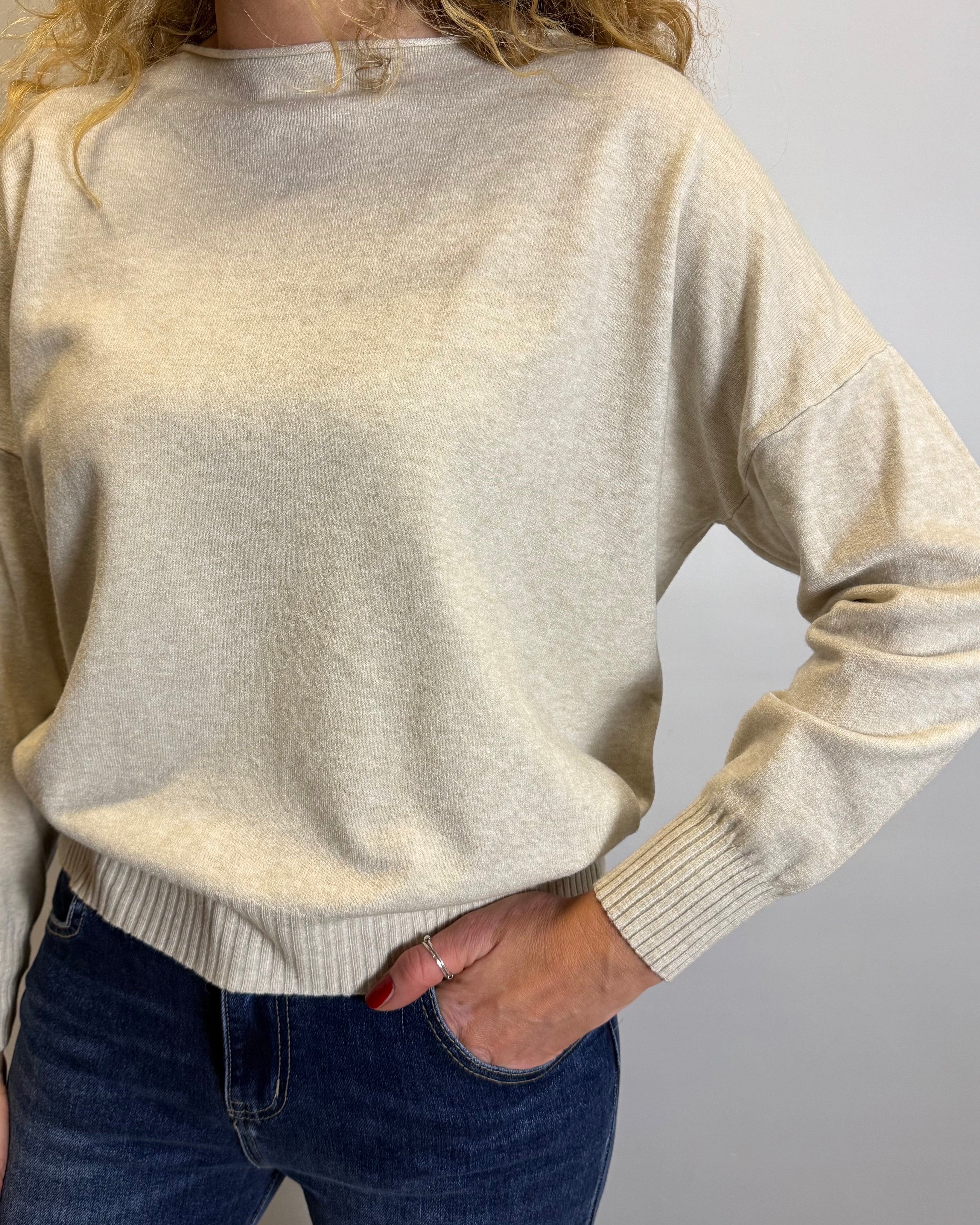 Person wearing a beige sweater and blue jeans against a plain background