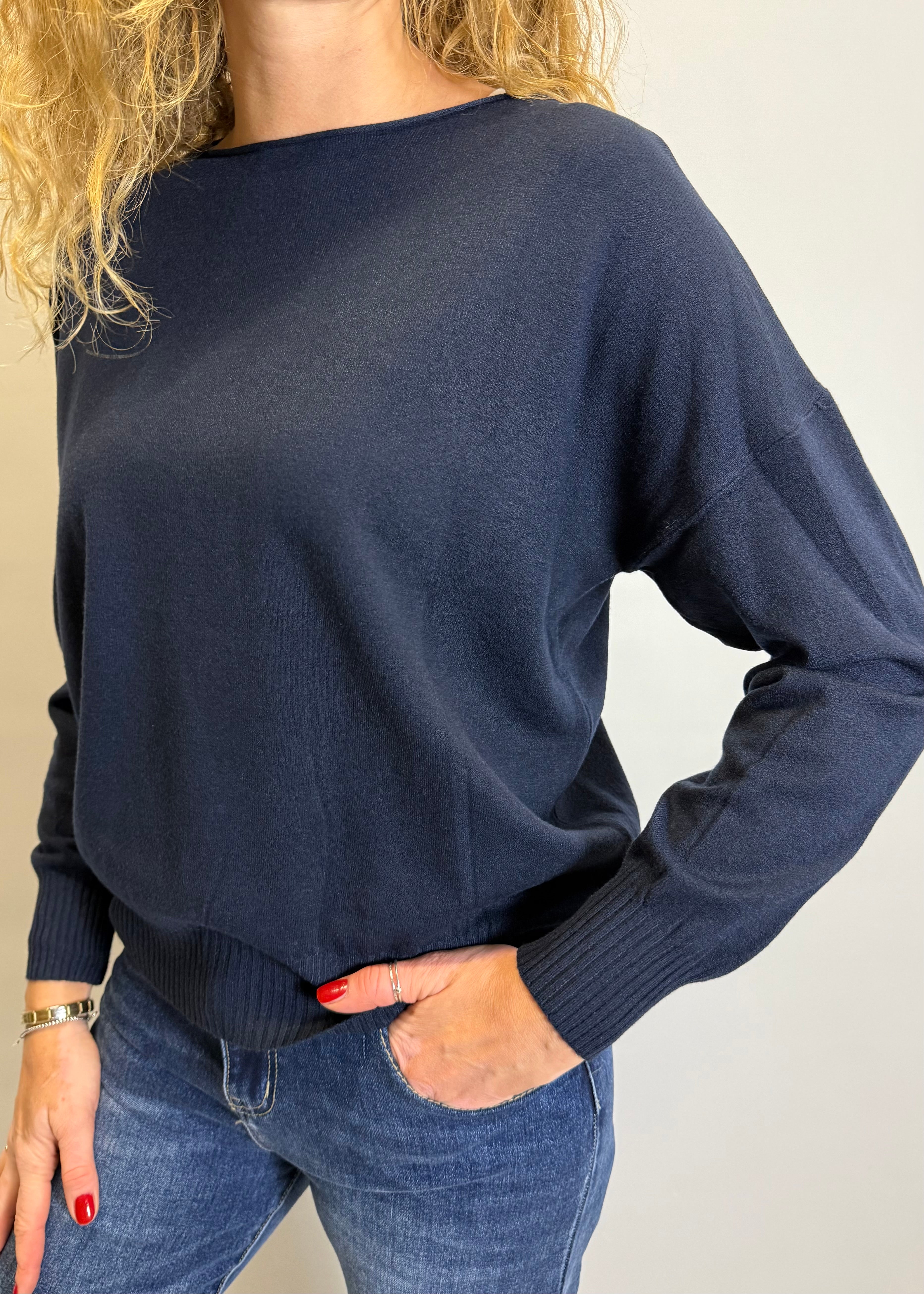 Person wearing a navy sweater and blue jeans against a plain background