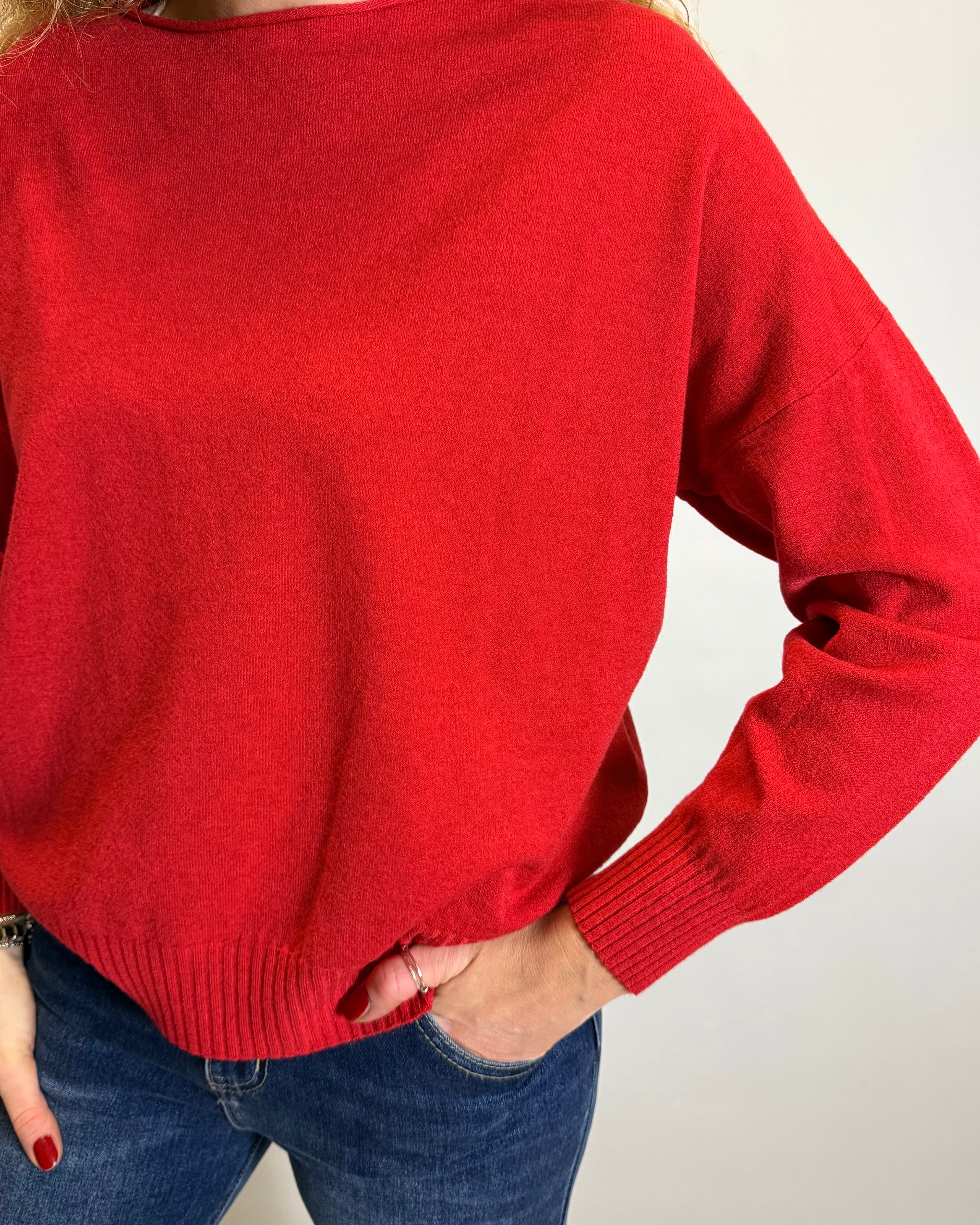 Person wearing a red sweater and blue jeans against a plain background