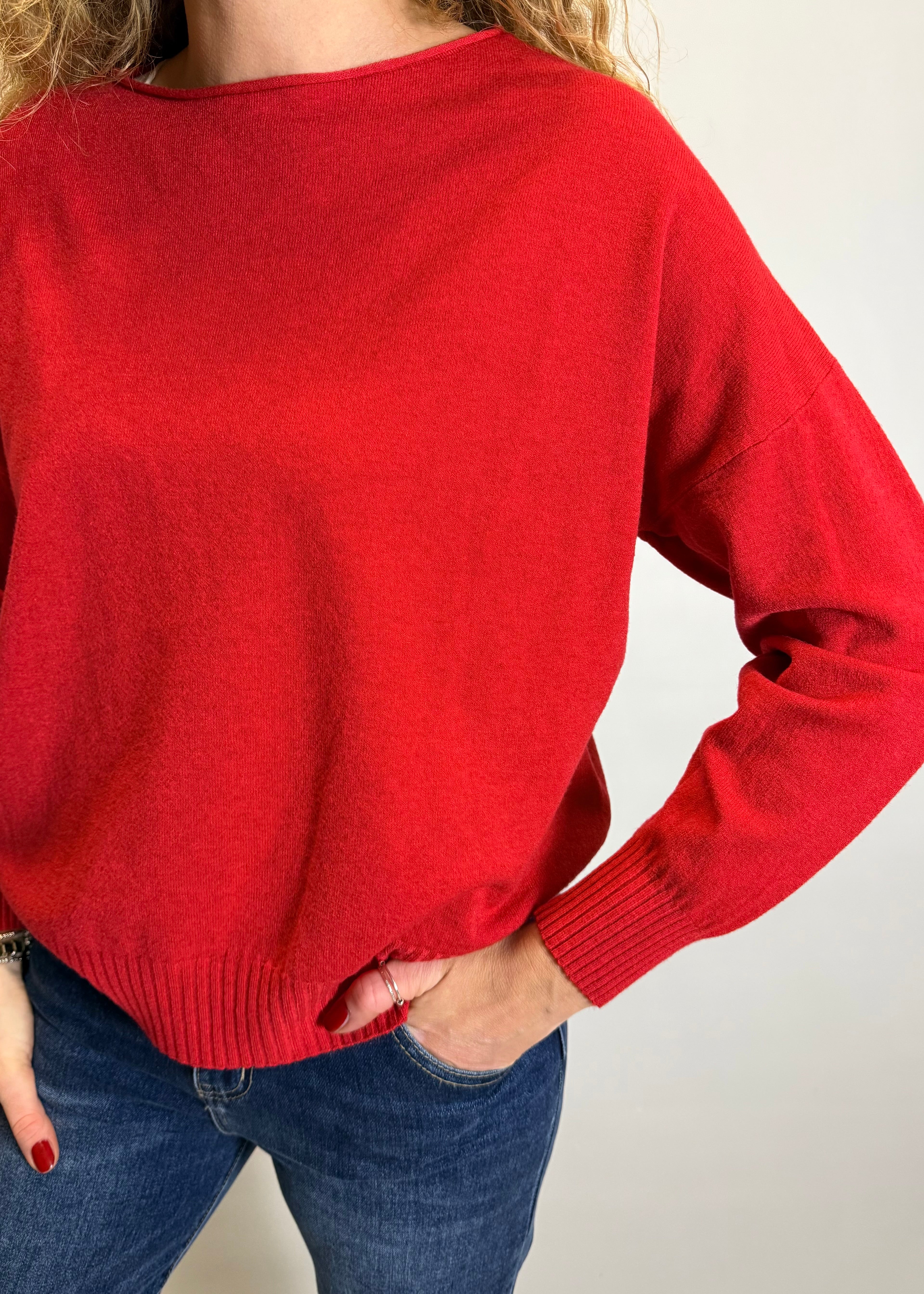 Person wearing a red sweater and blue jeans against a plain background