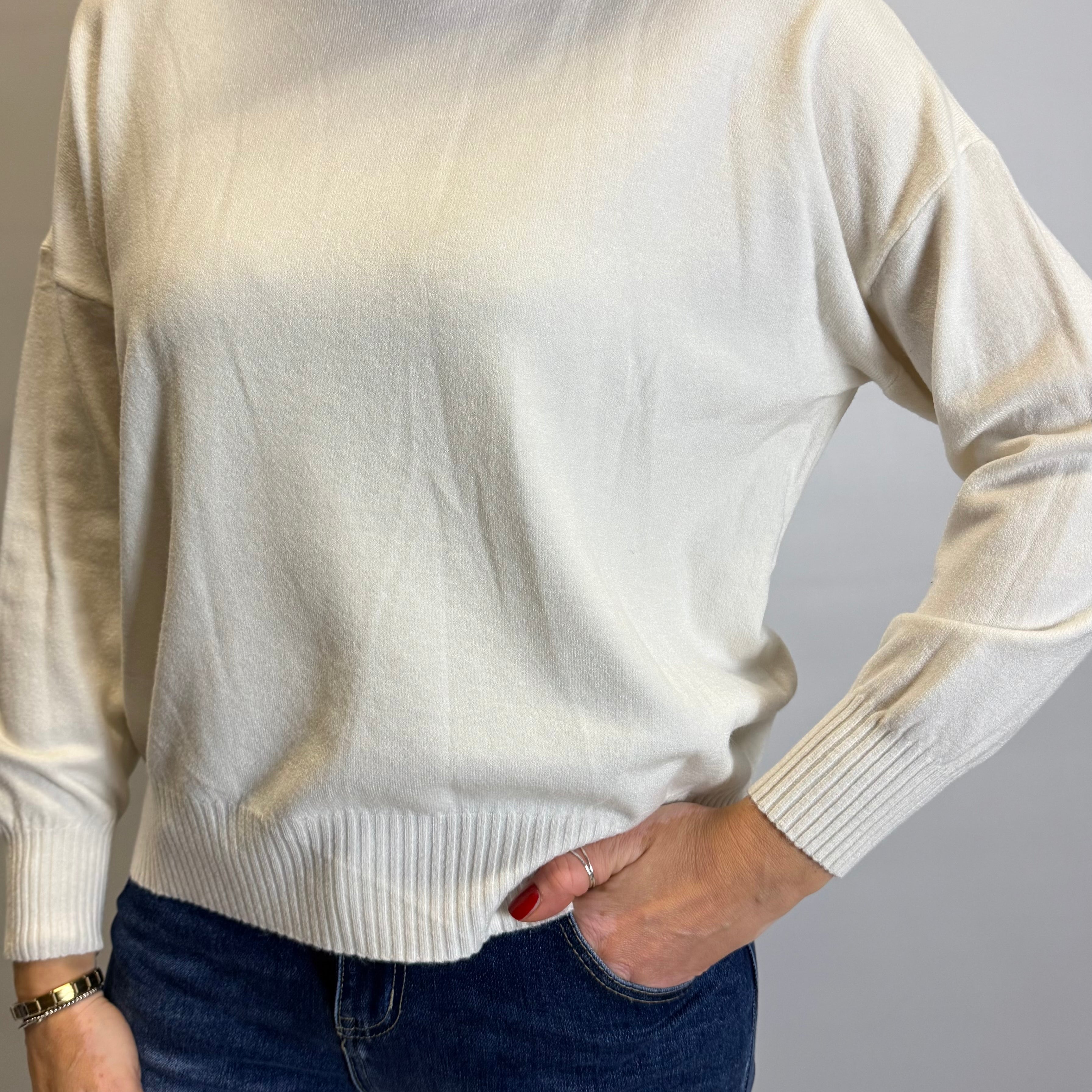 Person wearing a cream sweater and blue jeans against a plain background