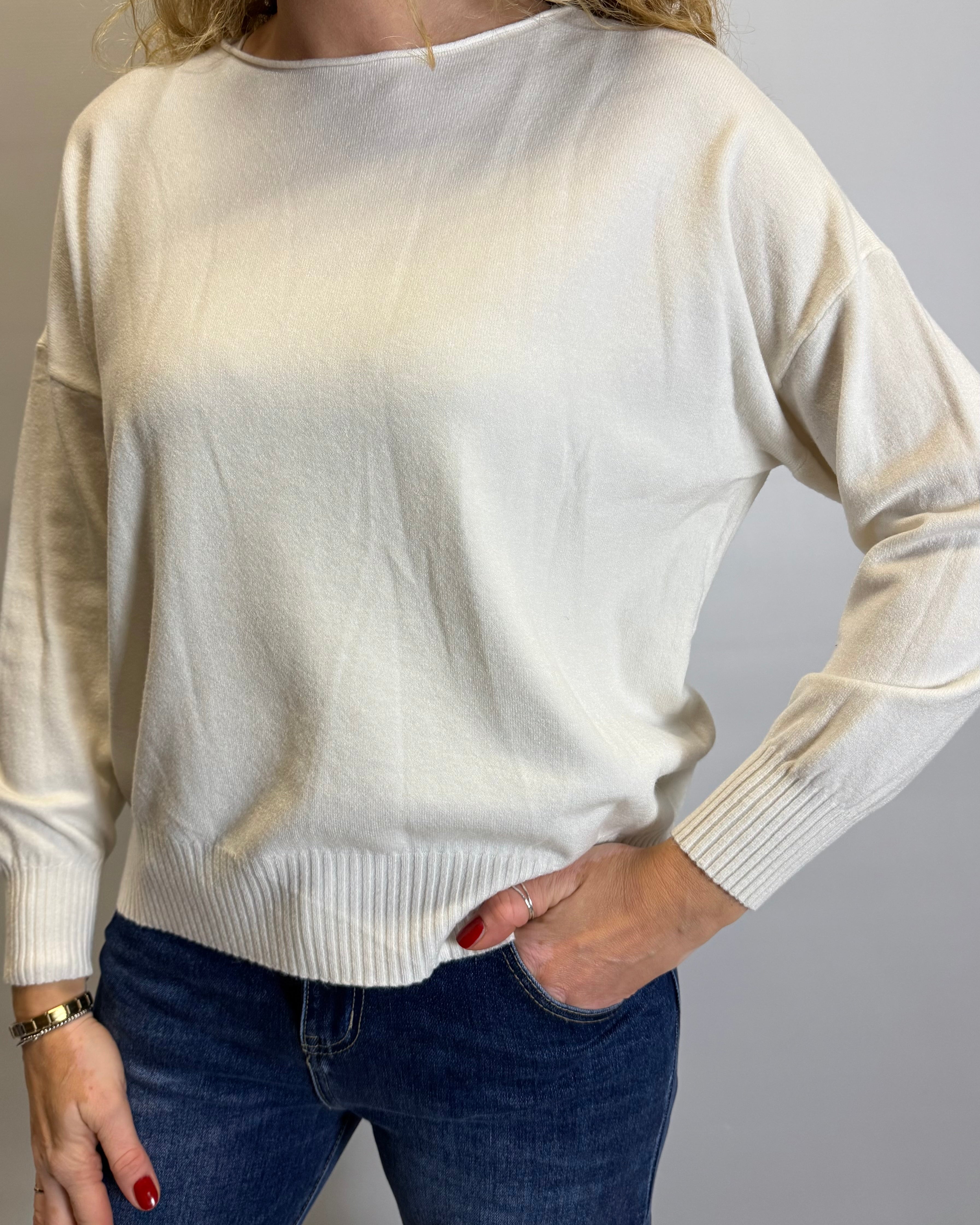 Person wearing a cream sweater and blue jeans against a plain background