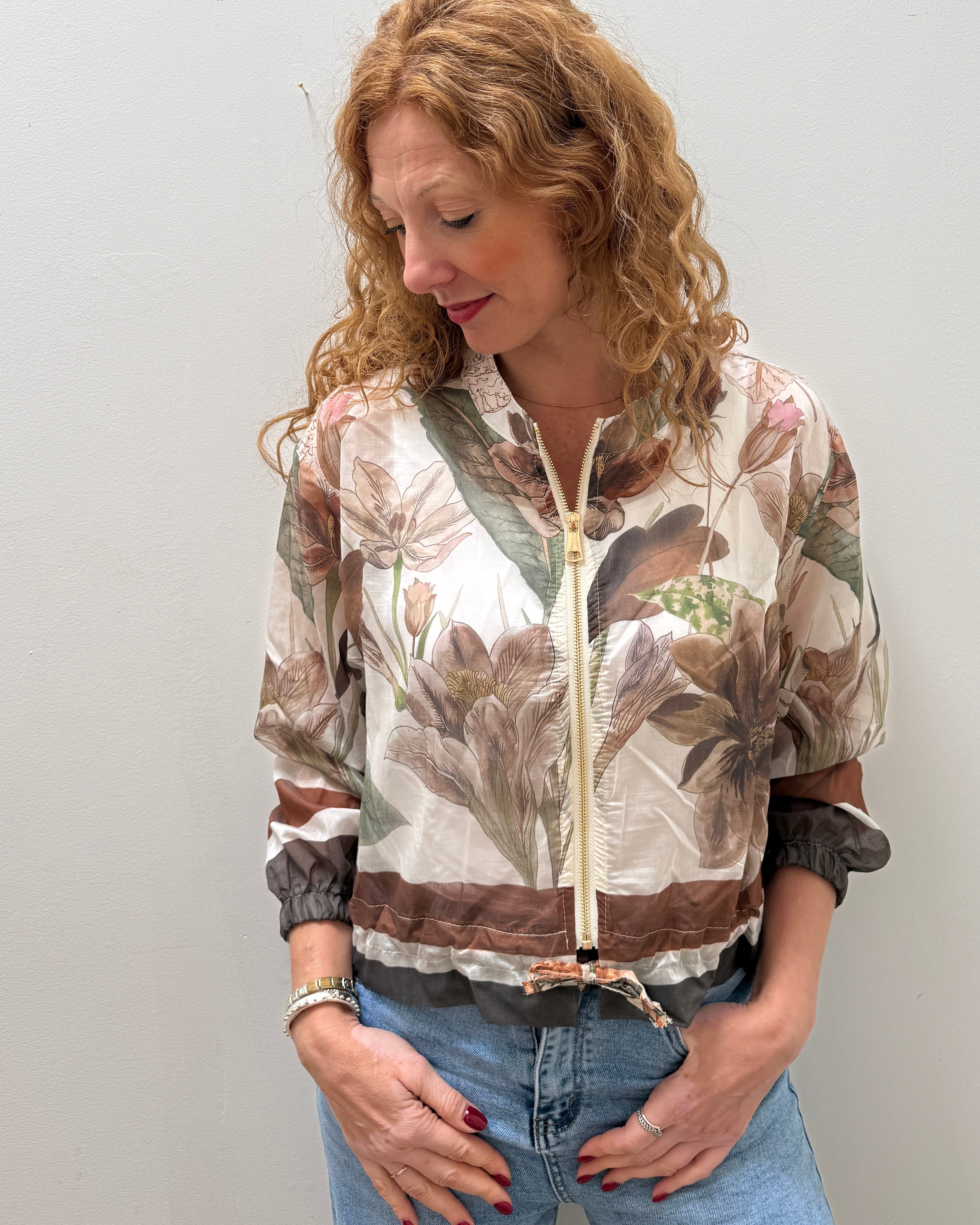 Person wearing a patterned jacket and jeans on a plain background
