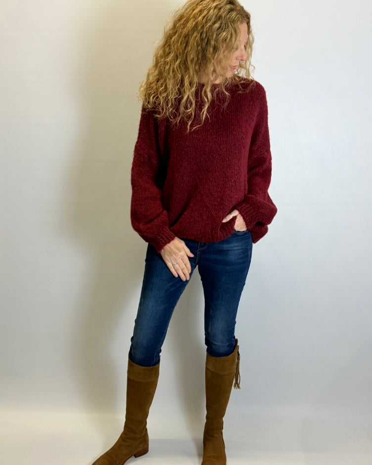 Person wearing a red sweater, blue jeans, and brown knee-high boots against a plain background
