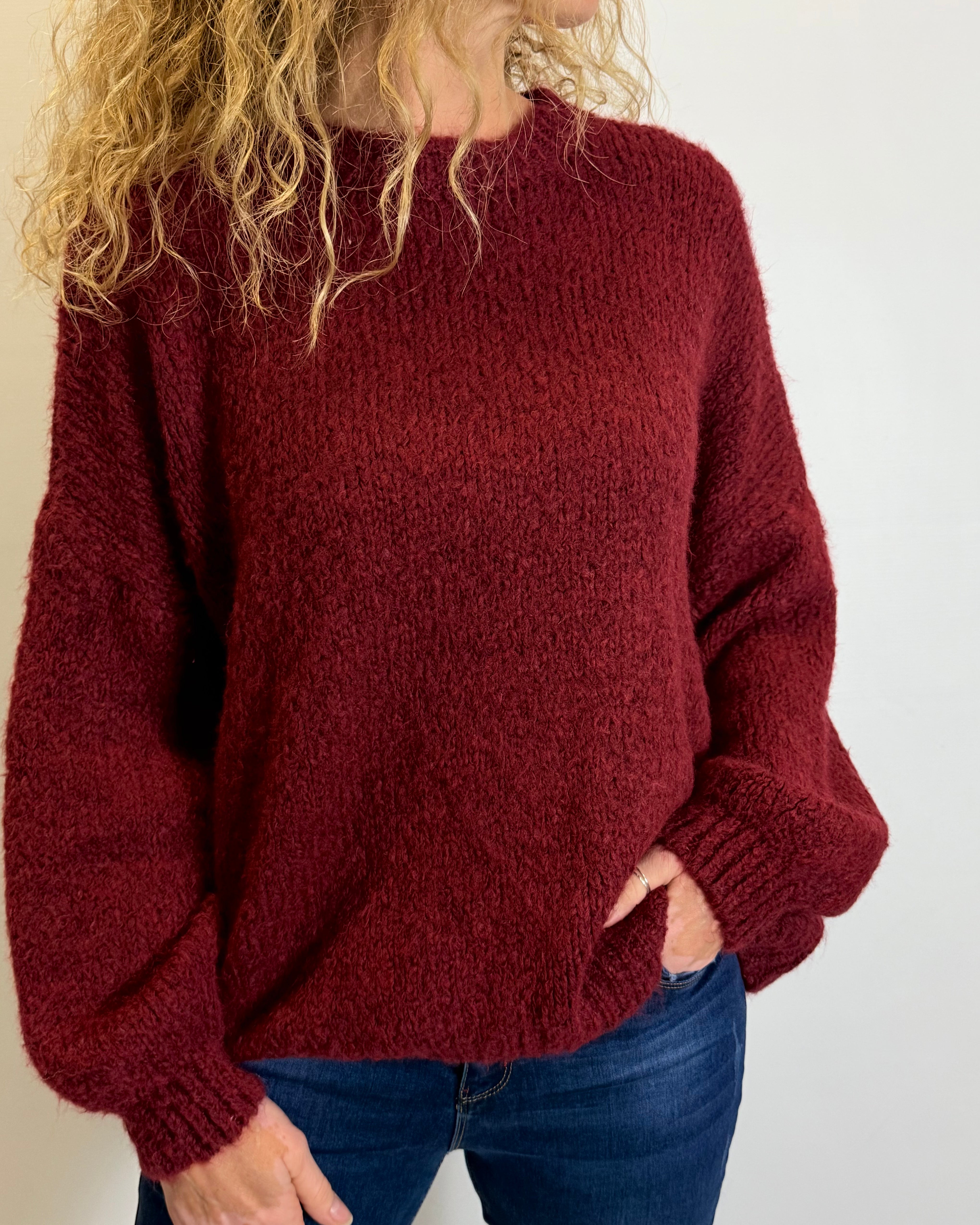 Person wearing a red sweater and blue jeans against a plain background
