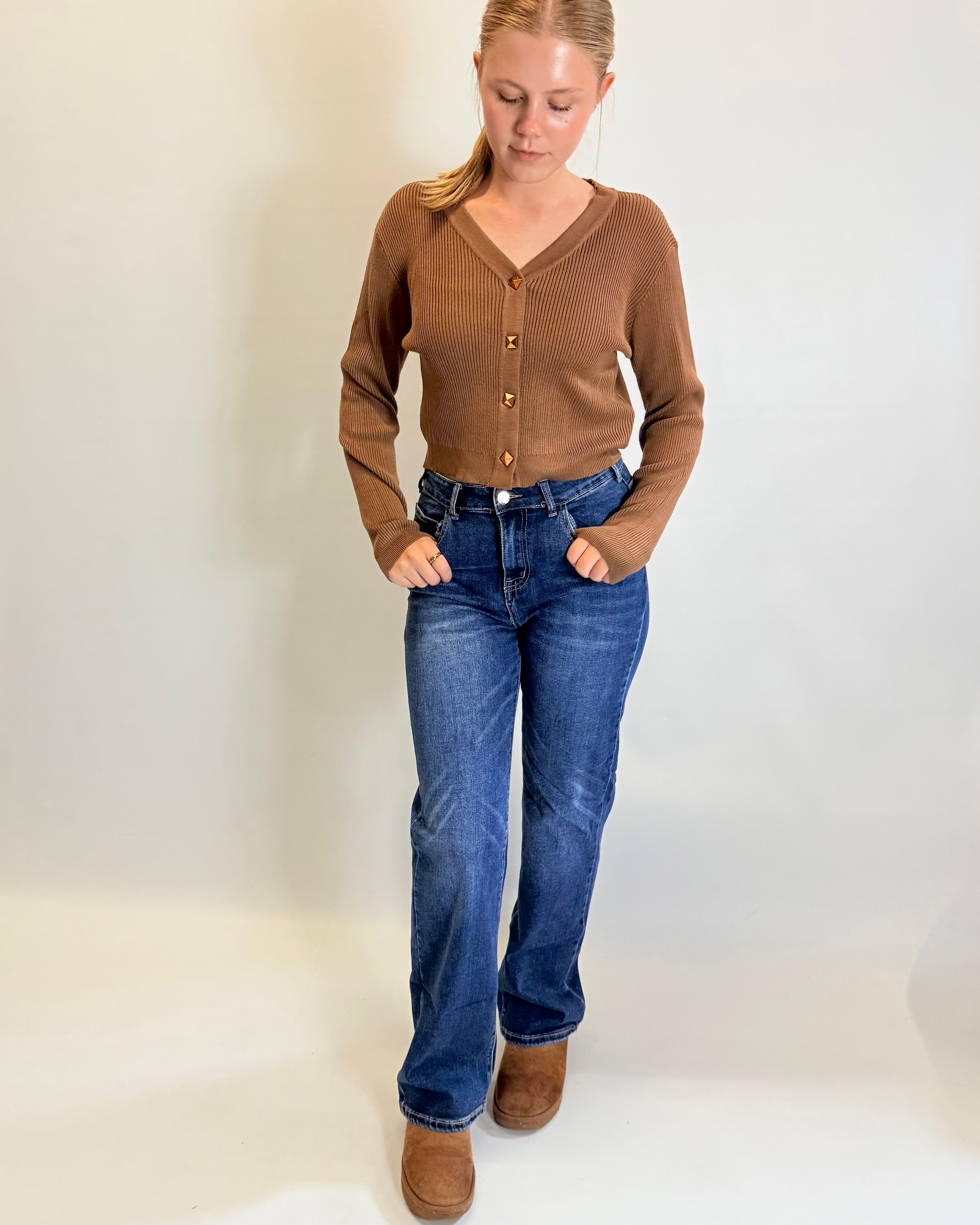 Woman wearing a brown cardigan, blue jeans, and brown boots on a white background