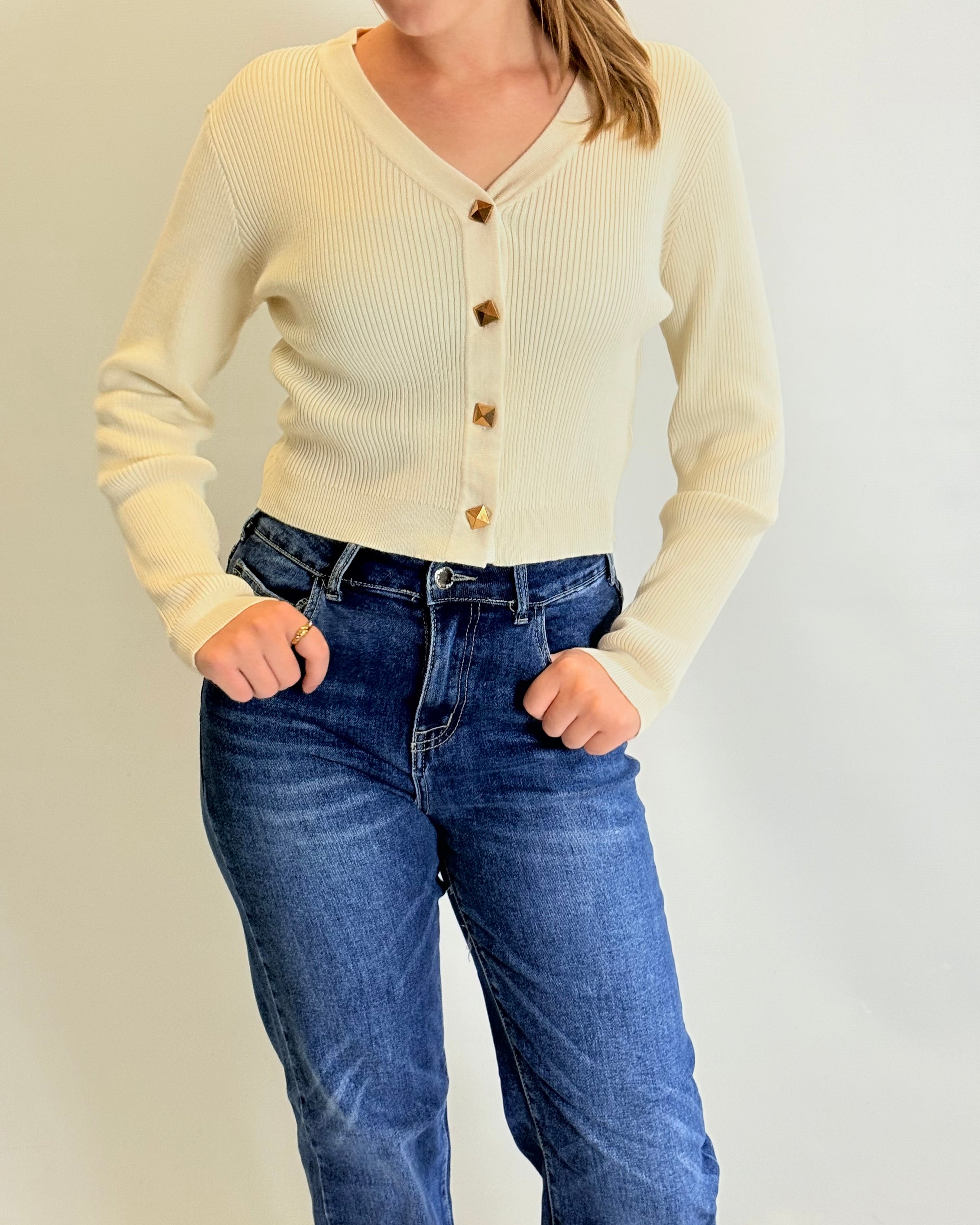 Person wearing a cream cardigan and blue jeans against a plain background