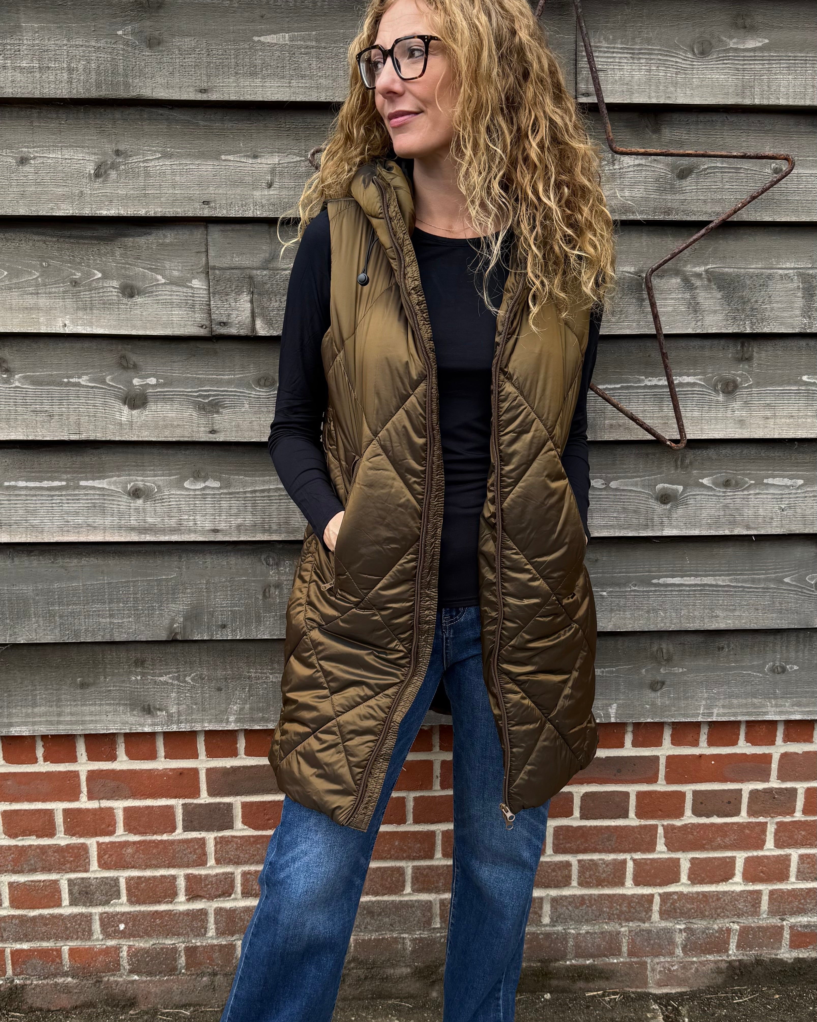 Woman wearing a green quilted vest against a wooden wall.