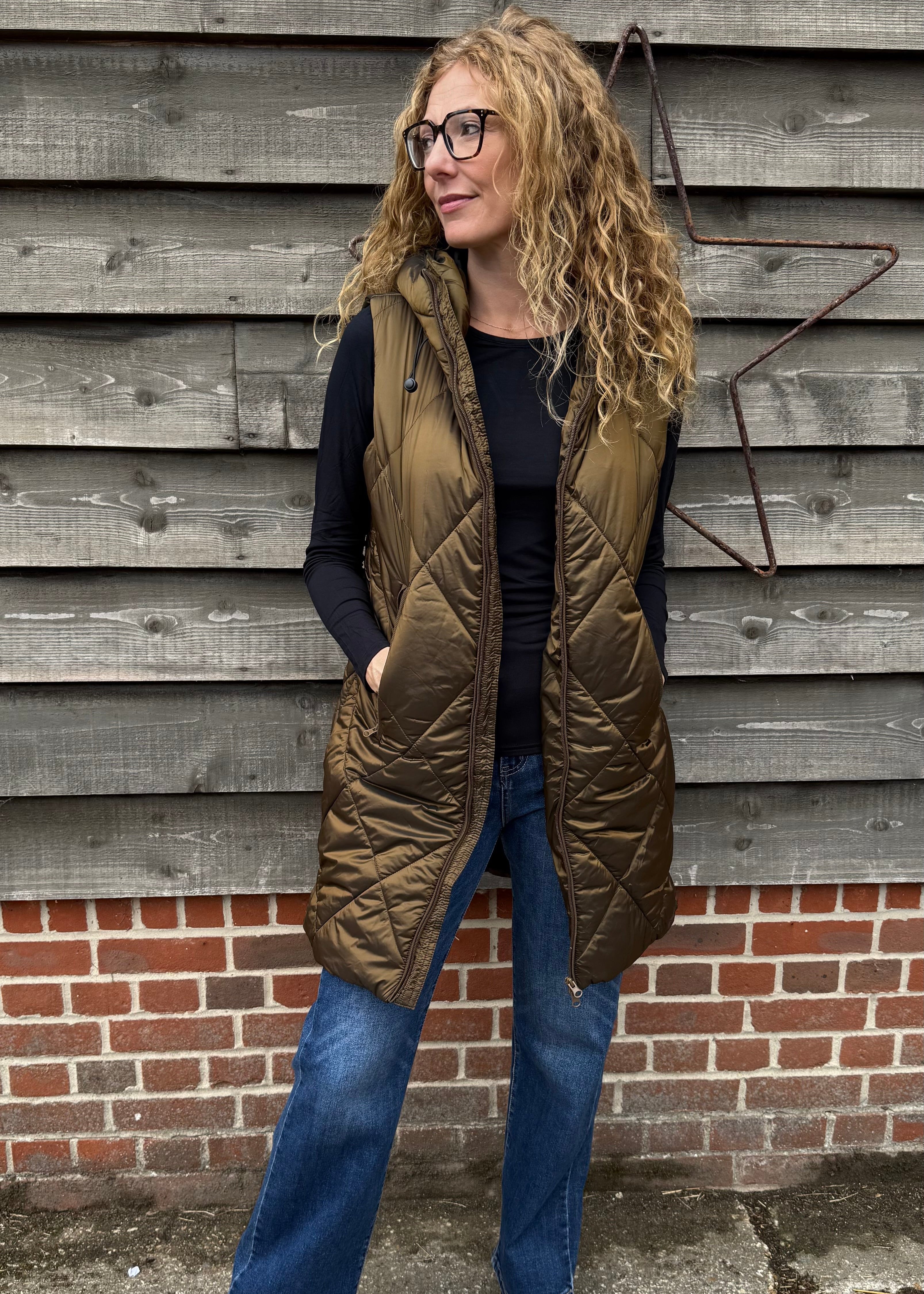 Woman wearing a green quilted vest against a wooden wall.