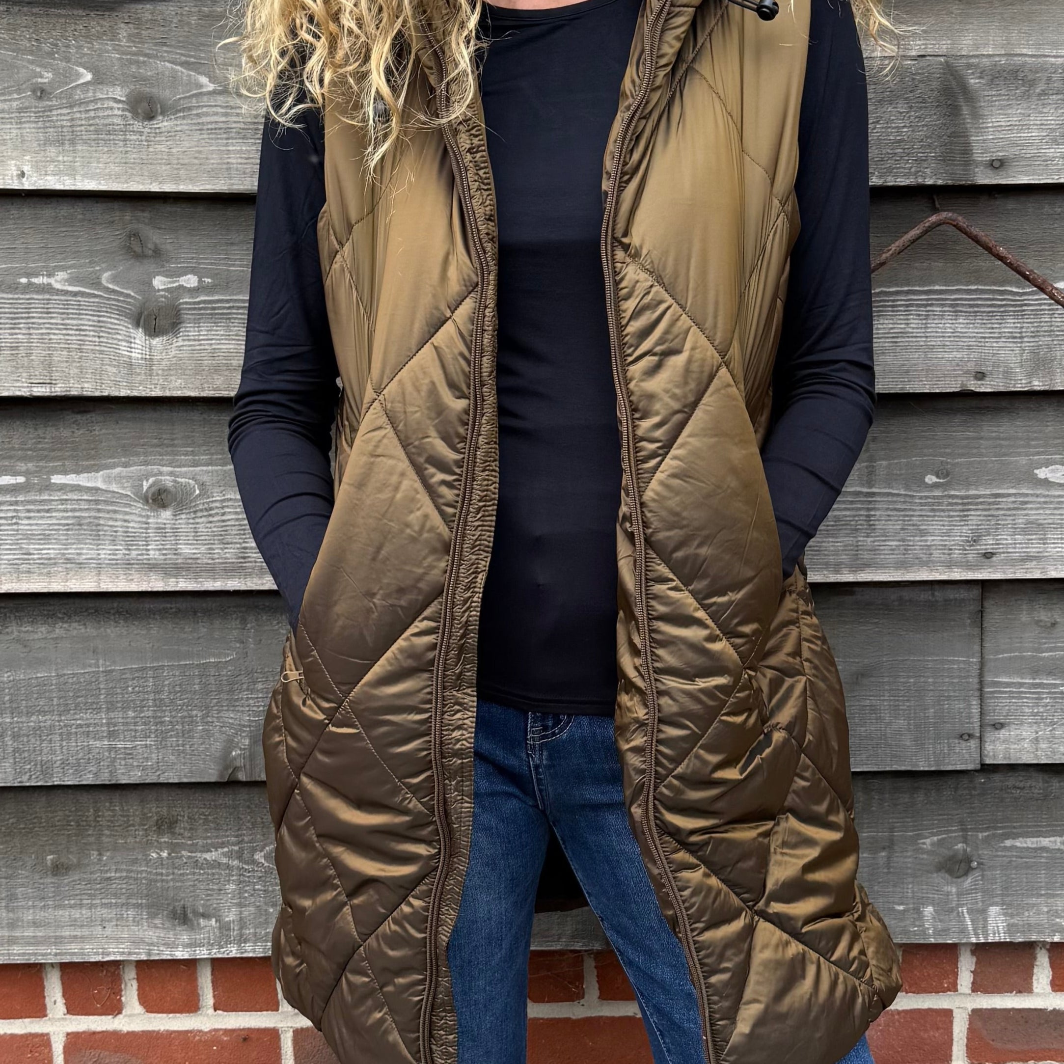 Woman wearing a green puffer vest standing against a wooden wall.