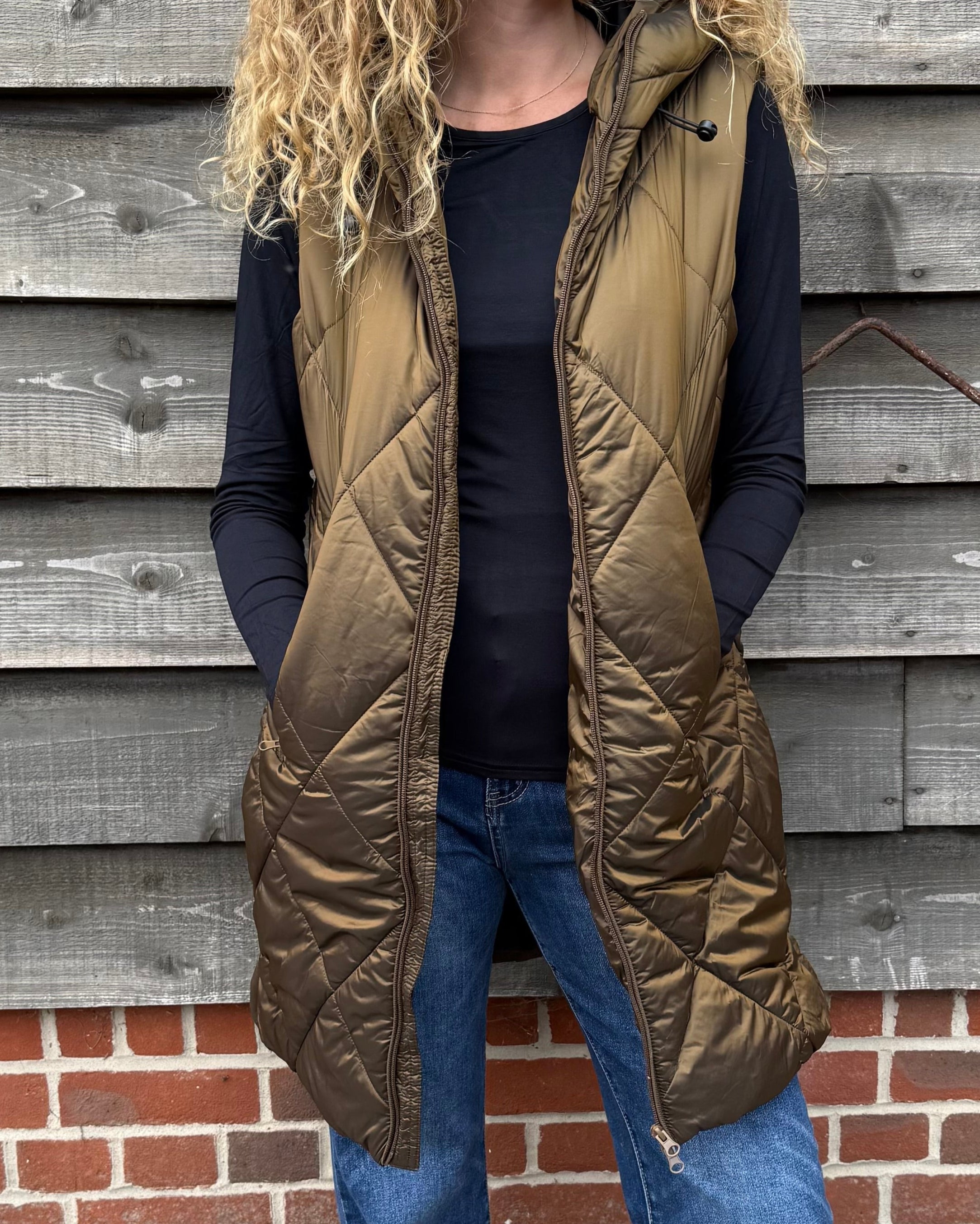 Woman wearing a green puffer vest standing against a wooden wall.