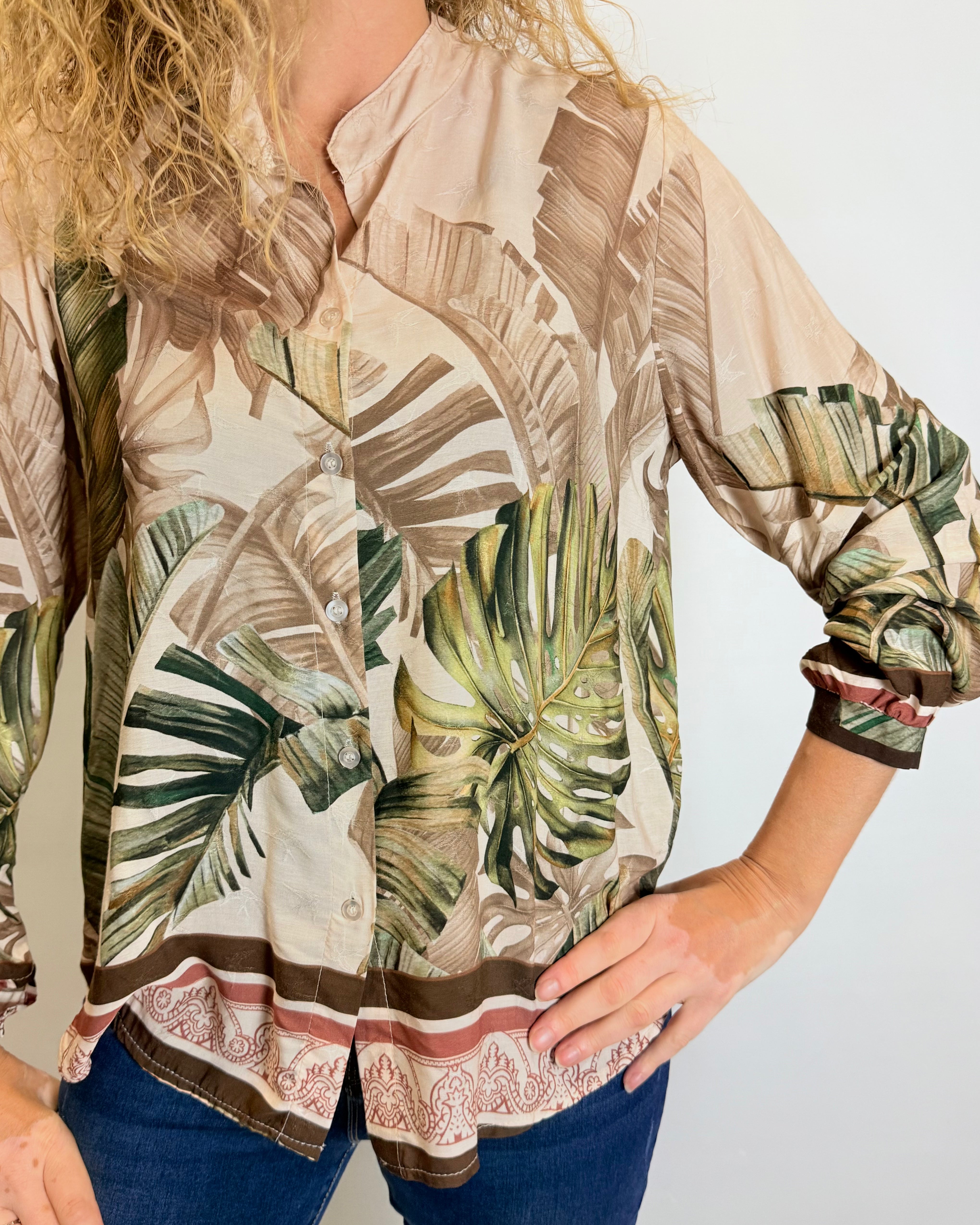 Woman wearing a tropical leaf patterned blouse with rolled-up sleeves against a plain background