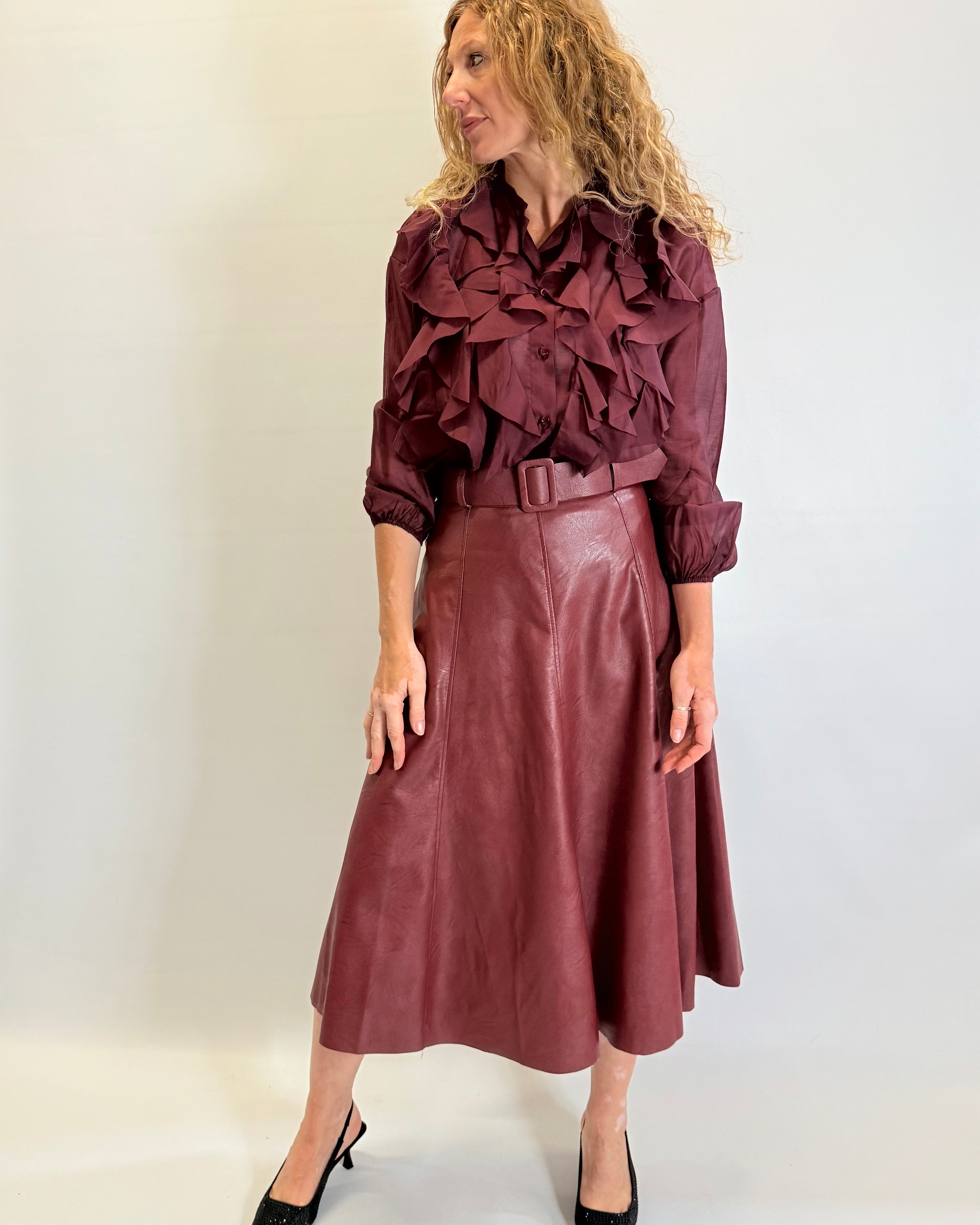 Woman wearing a burgundy ruffled blouse and leather skirt against a white background