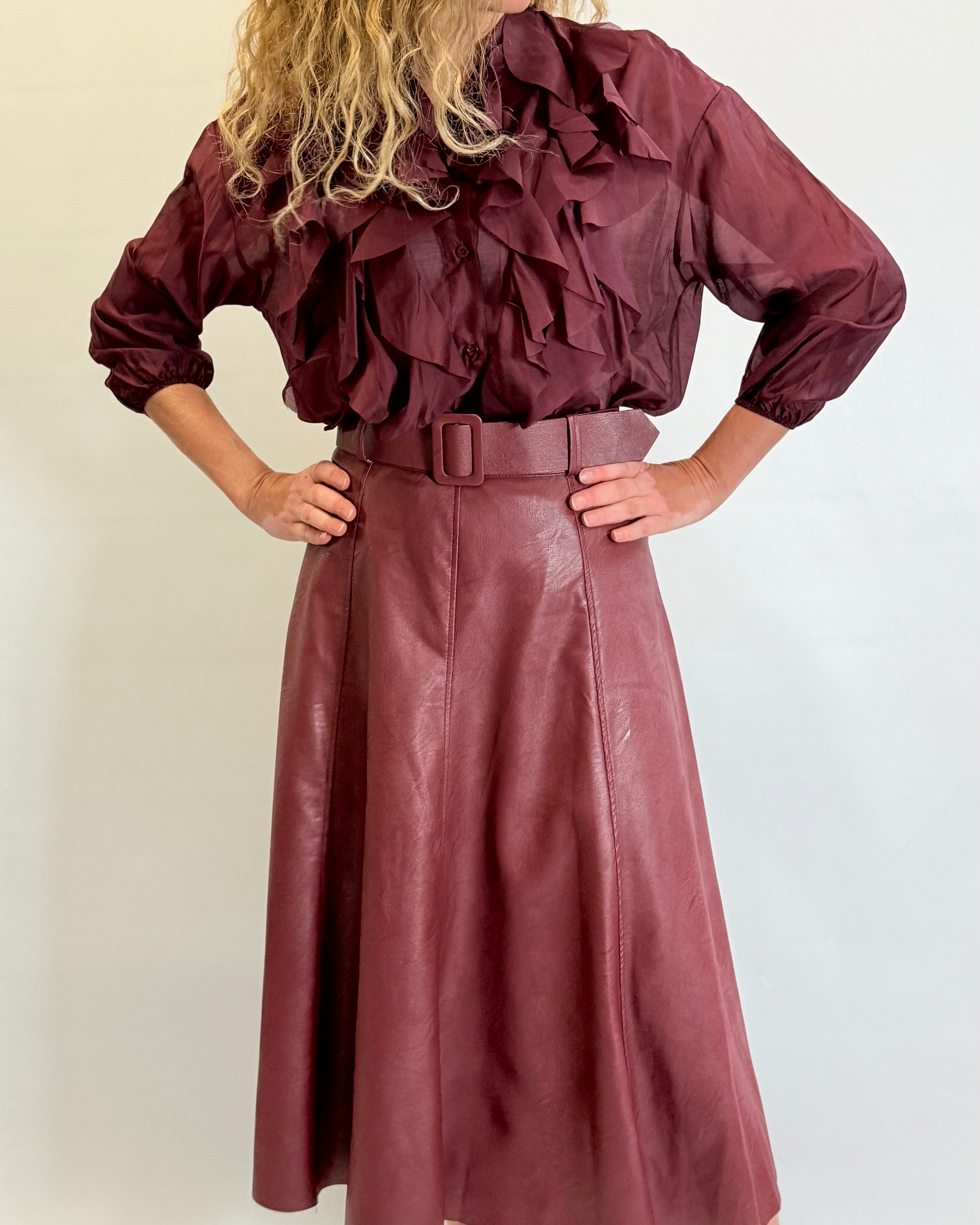 Person wearing a burgundy ruffled blouse and leather skirt against a plain background