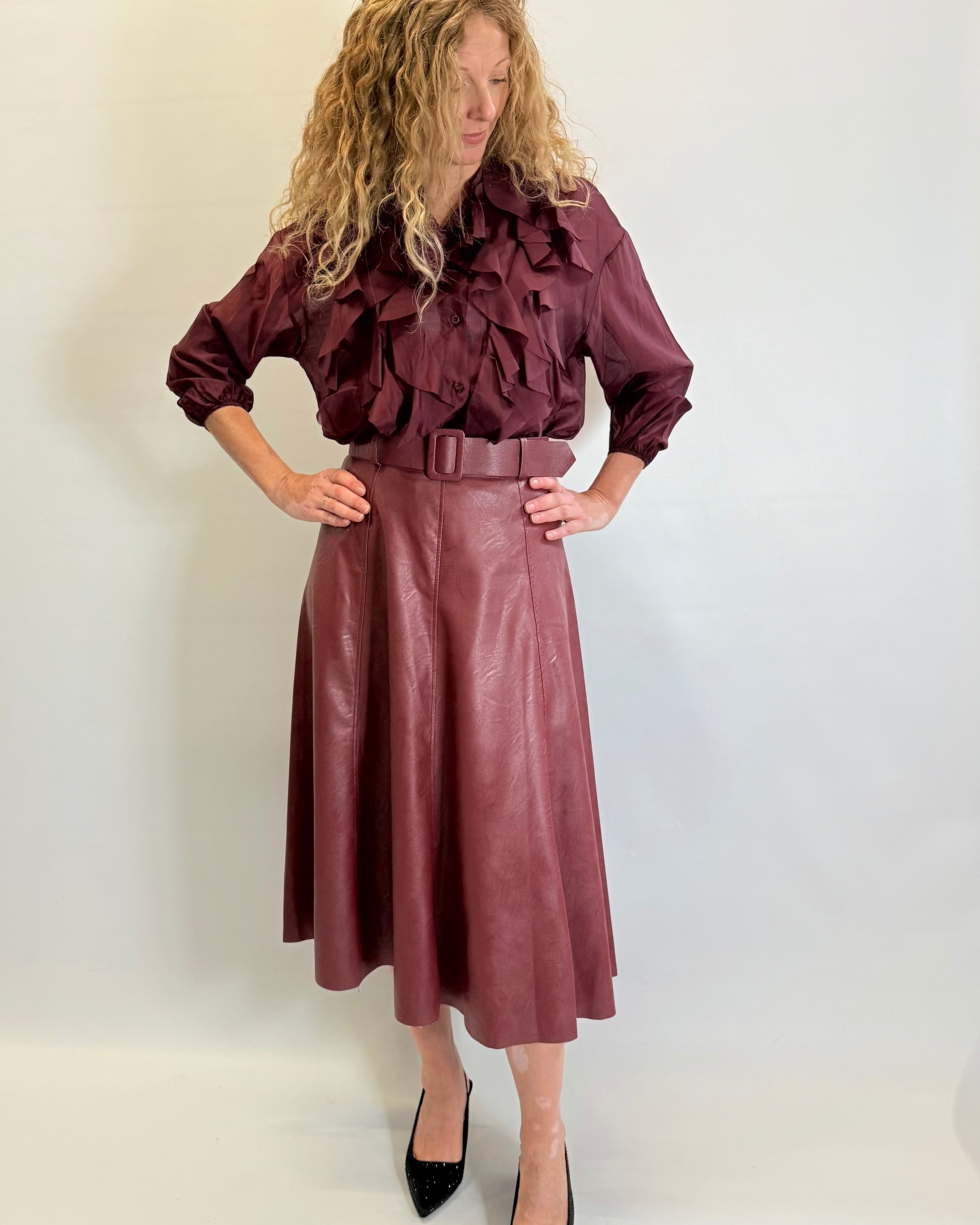 Woman wearing a burgundy ruffled blouse and leather skirt against a white background