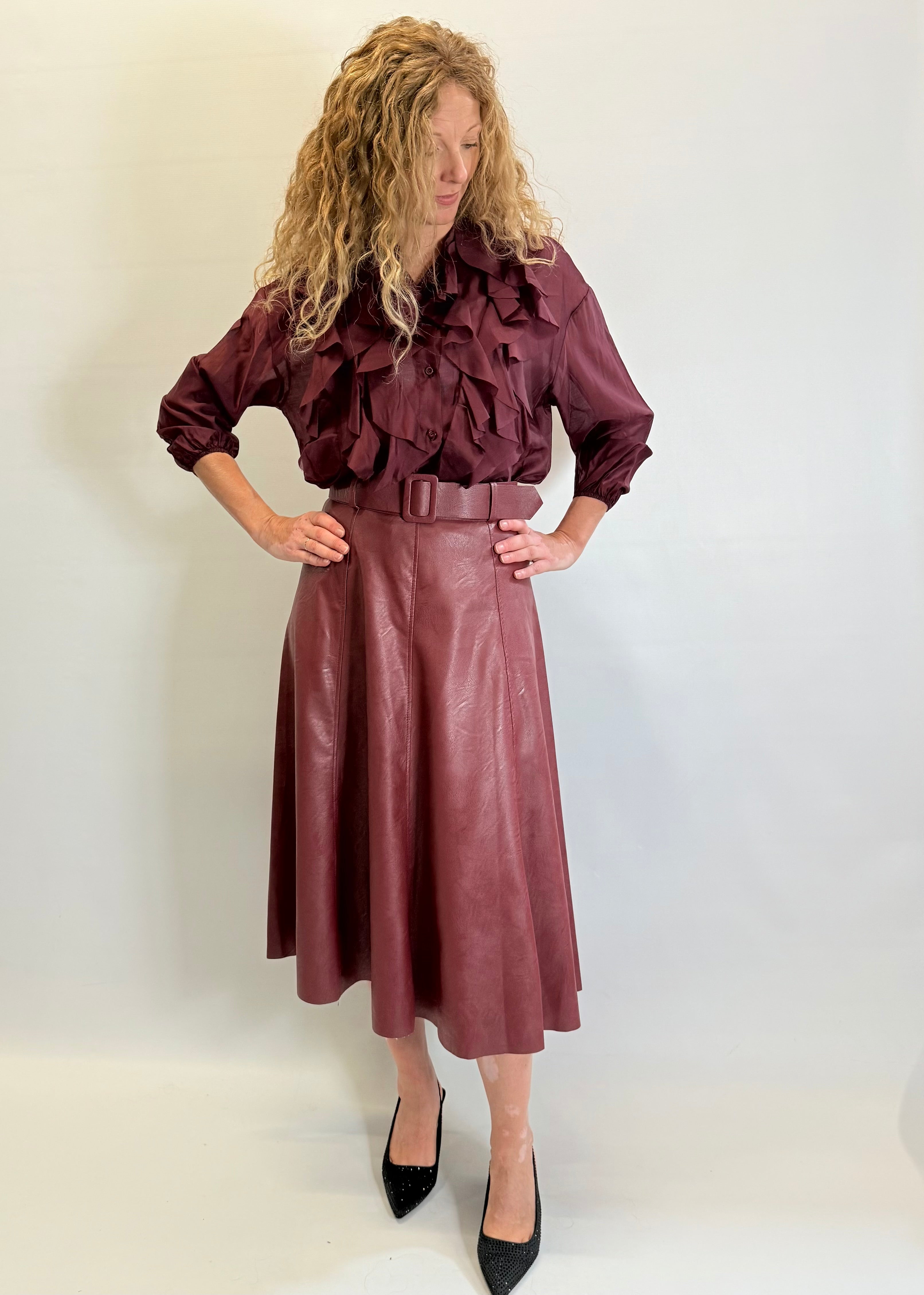 Woman wearing a burgundy ruffled blouse and leather skirt against a white background