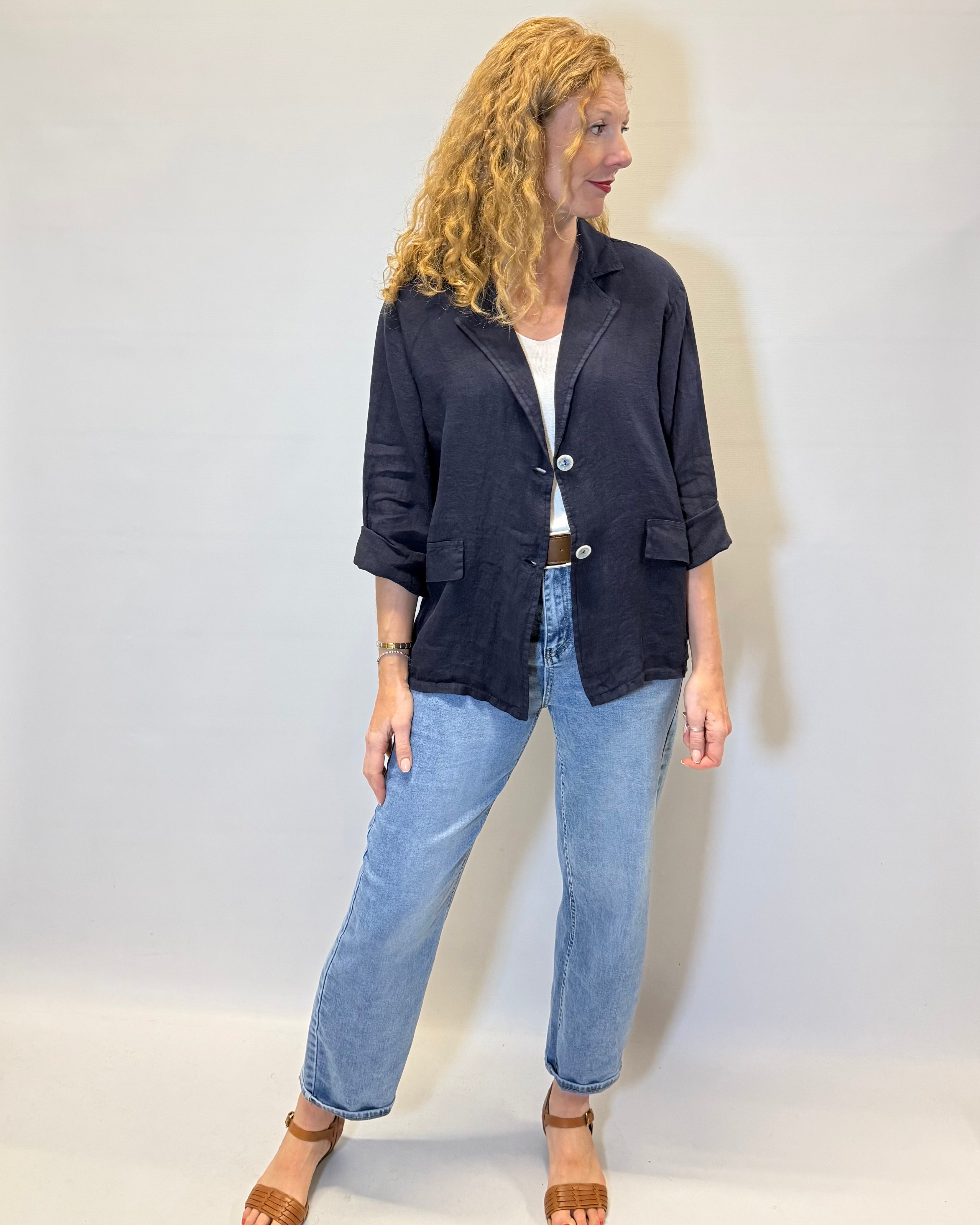 Woman wearing a dark jacket and light blue jeans against a white background