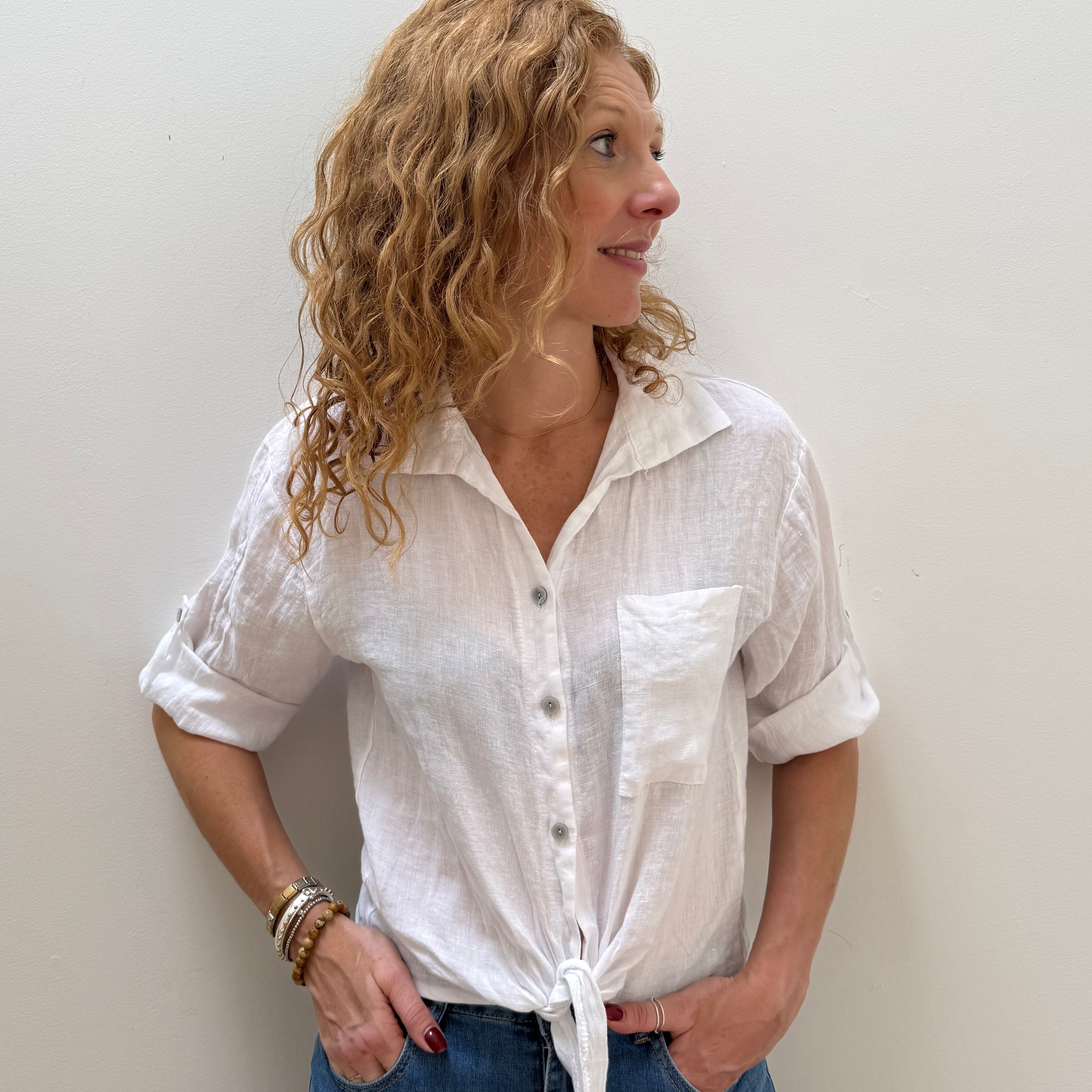 Woman wearing a white button-up shirt and blue jeans against a plain background
