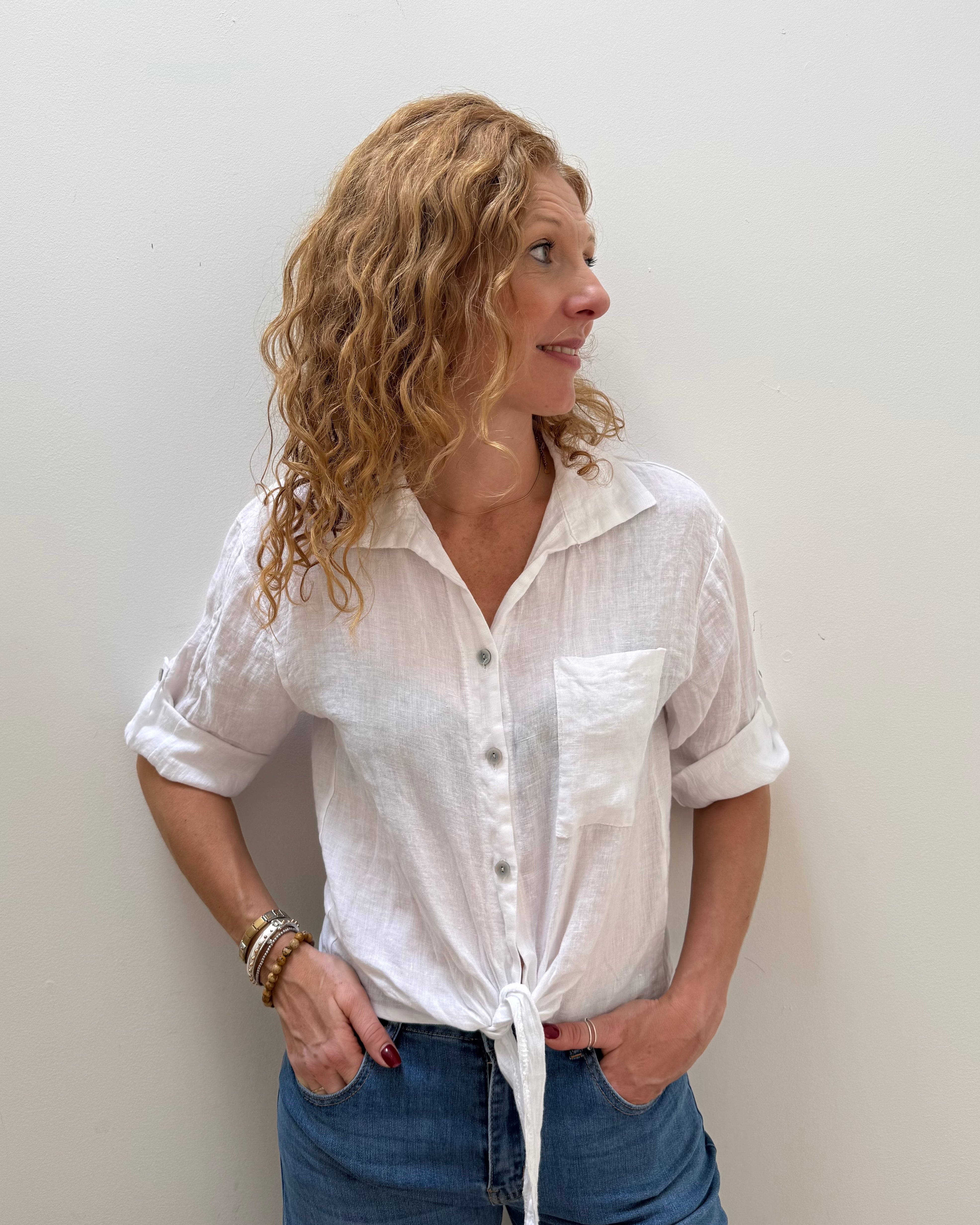Woman wearing a white button-up shirt and blue jeans against a plain background