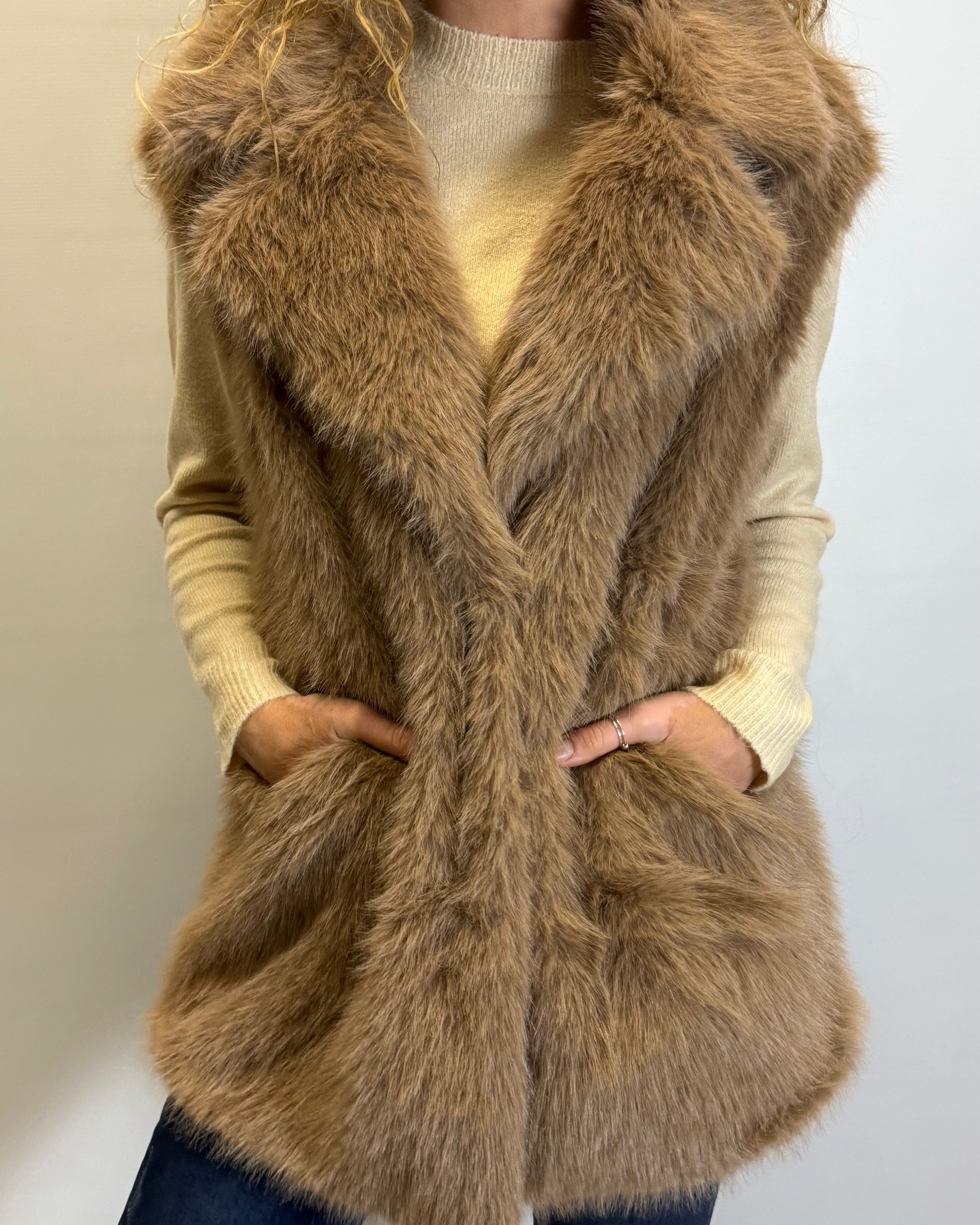 Person wearing a brown fur vest over a beige sweater on a plain background