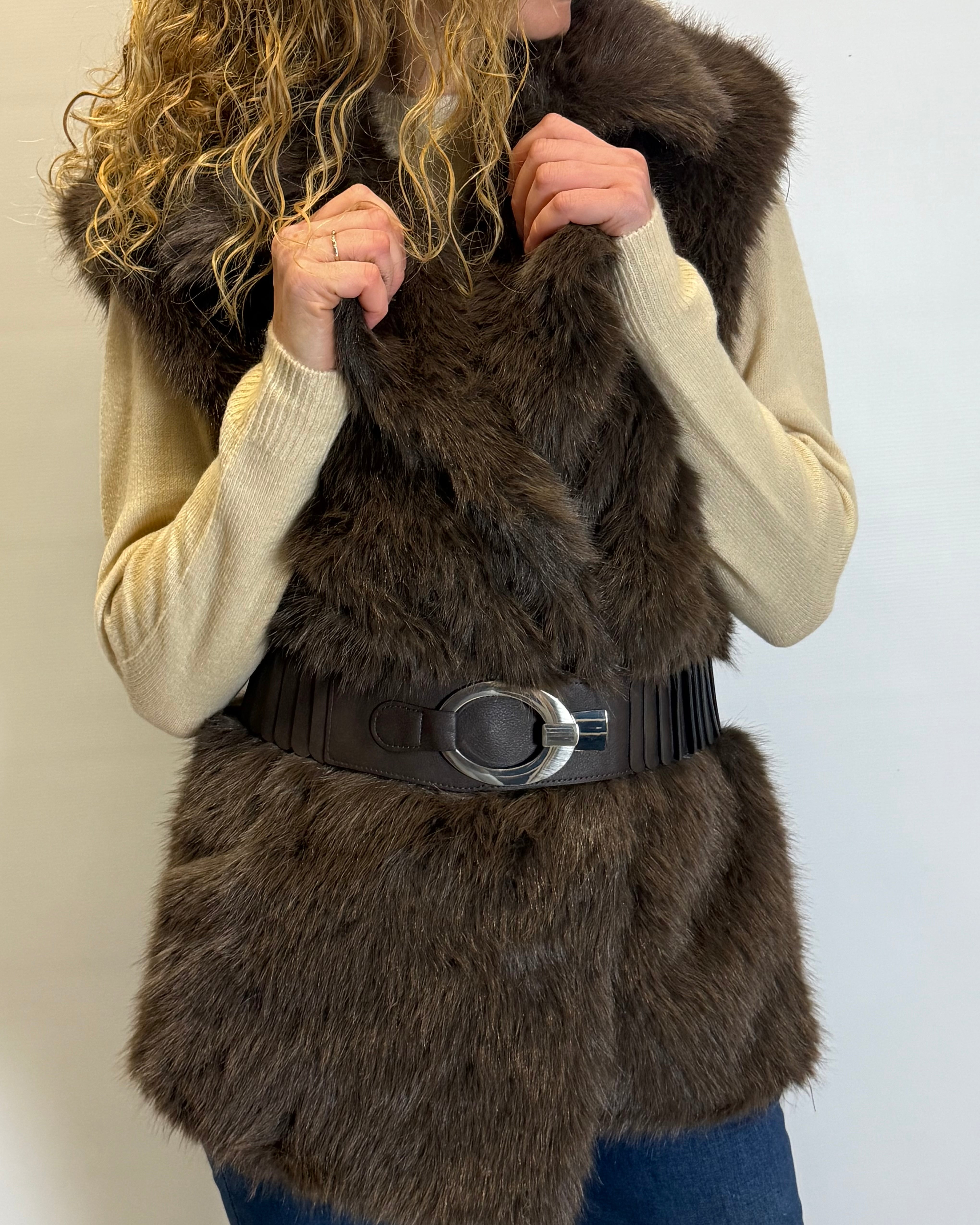 Person wearing a brown fur vest with a black belt against a white background