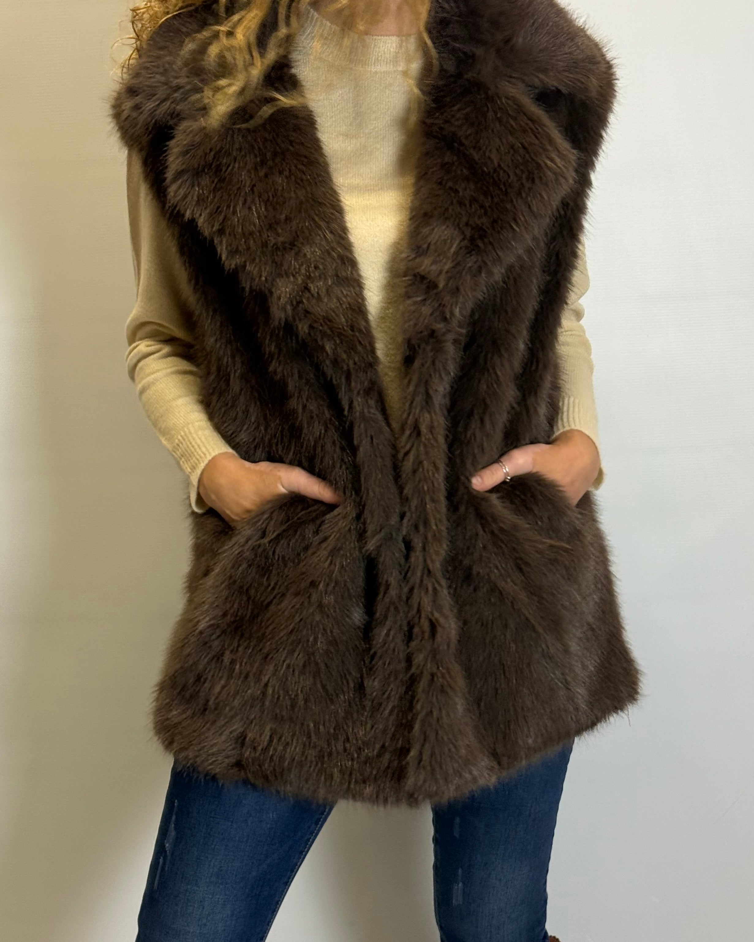 Person wearing a brown fur vest against a plain background