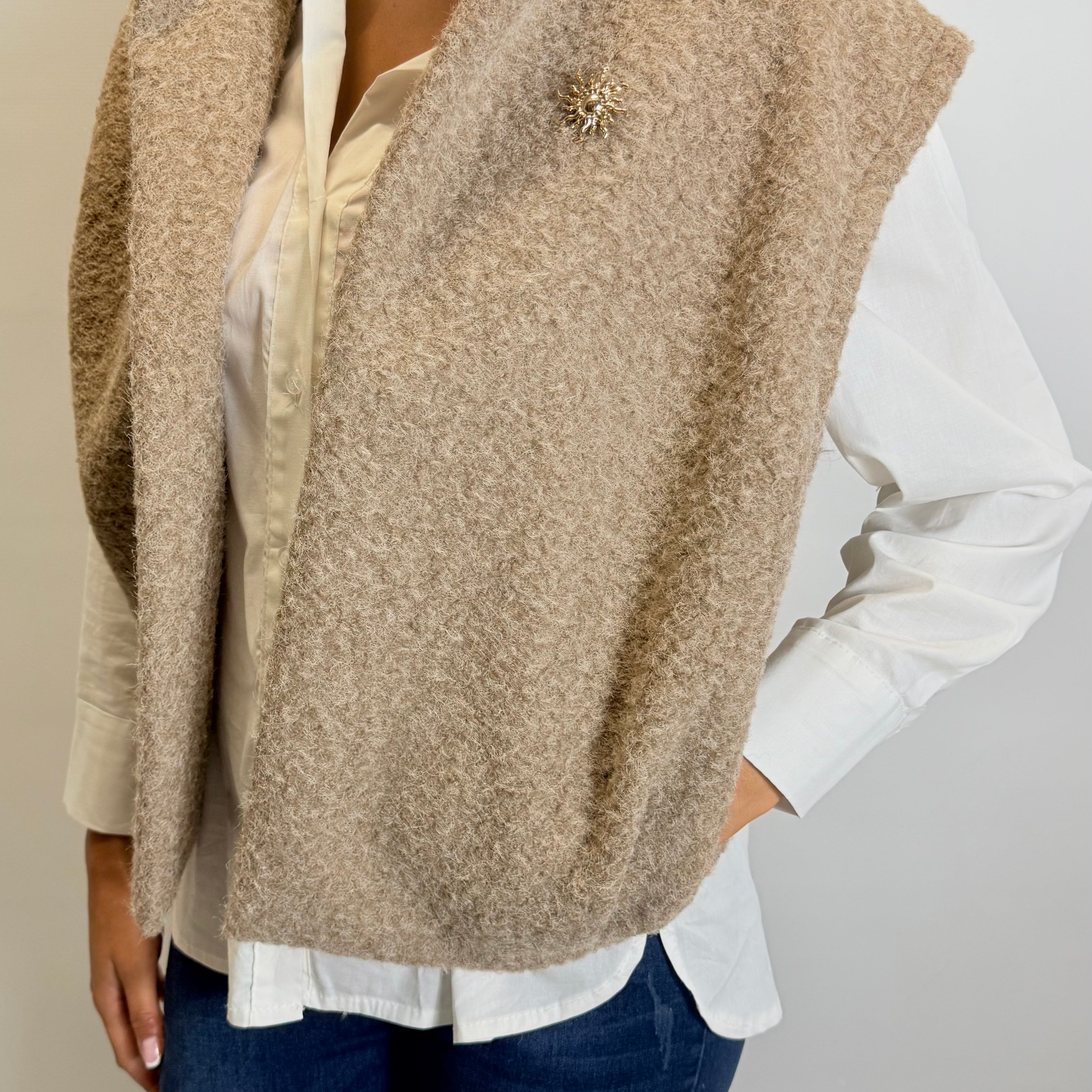 Person wearing a beige vest over a white shirt and blue jeans on a plain background