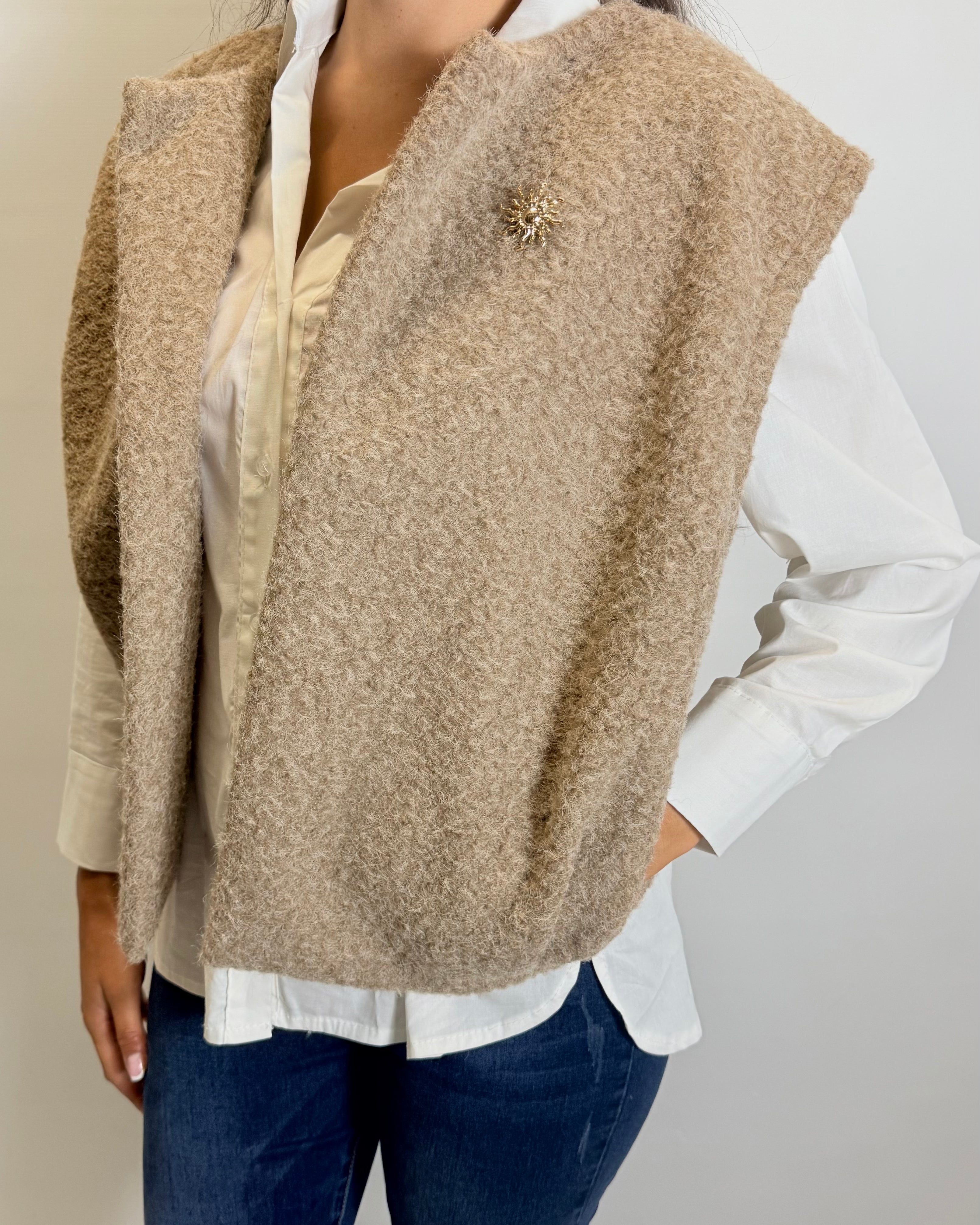 Person wearing a beige vest over a white shirt and blue jeans on a plain background